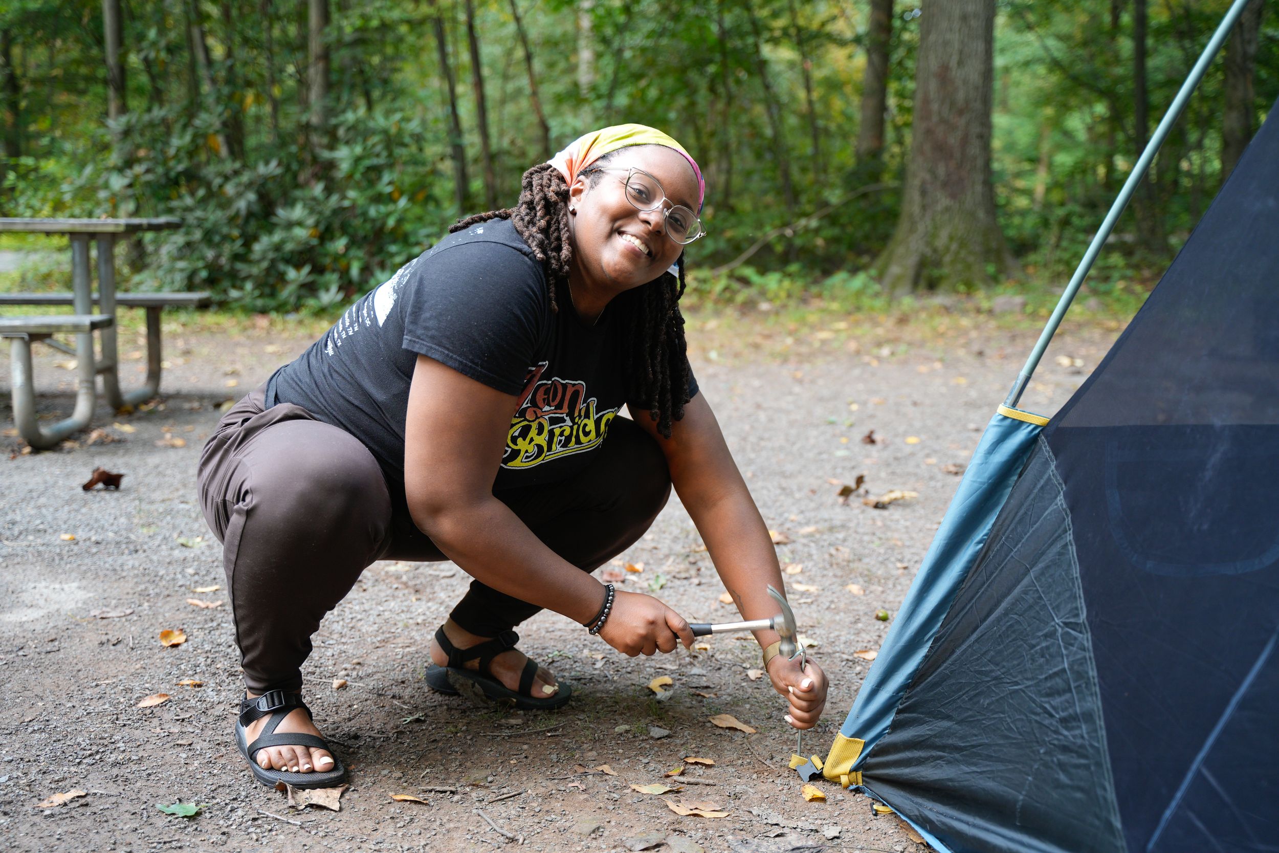 Woman crouching to stake a tent at a forest campground.