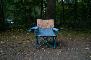 Blue folding camp chair sitting on dirt ground in a wooded forest campsite.