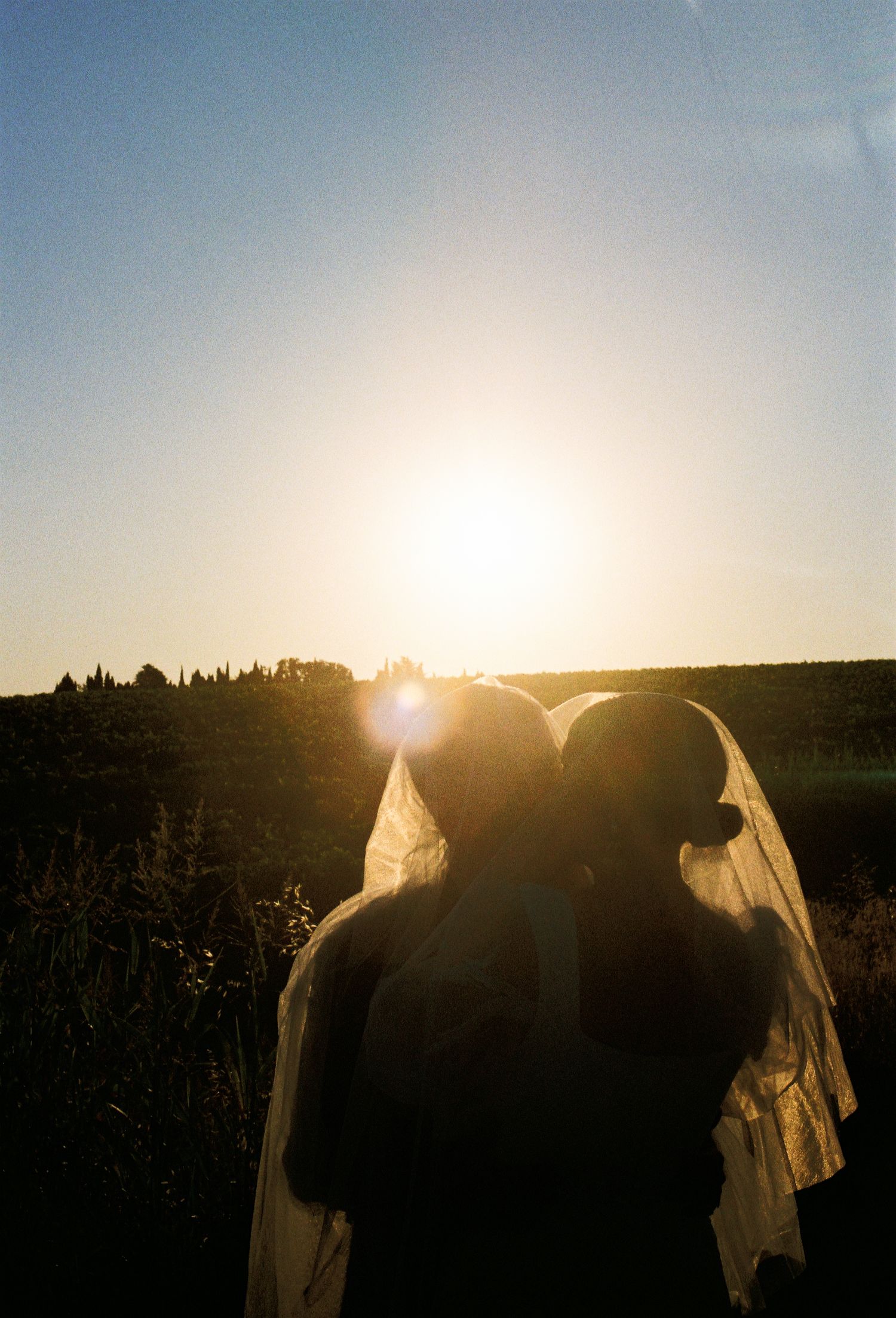 Silhouette of a bride and groom kissing against a stunning golden sunset in an open field.