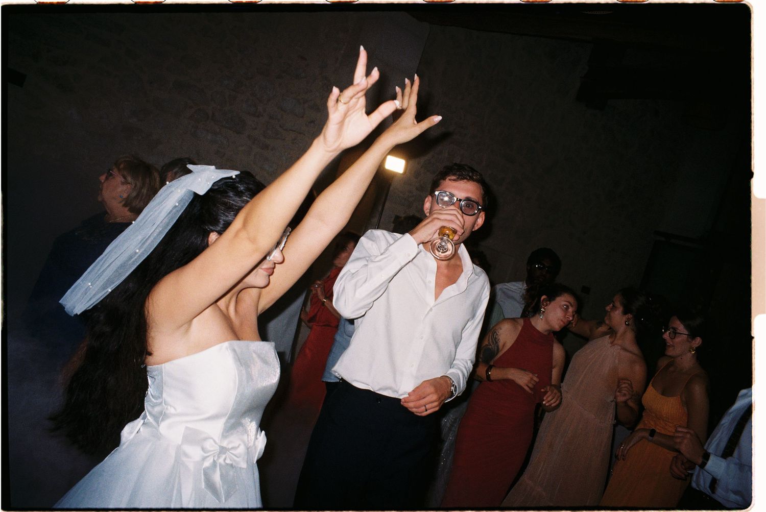 Bride and groom dancing joyfully at wedding reception, woman in white dress raises arms while man sings into microphone.