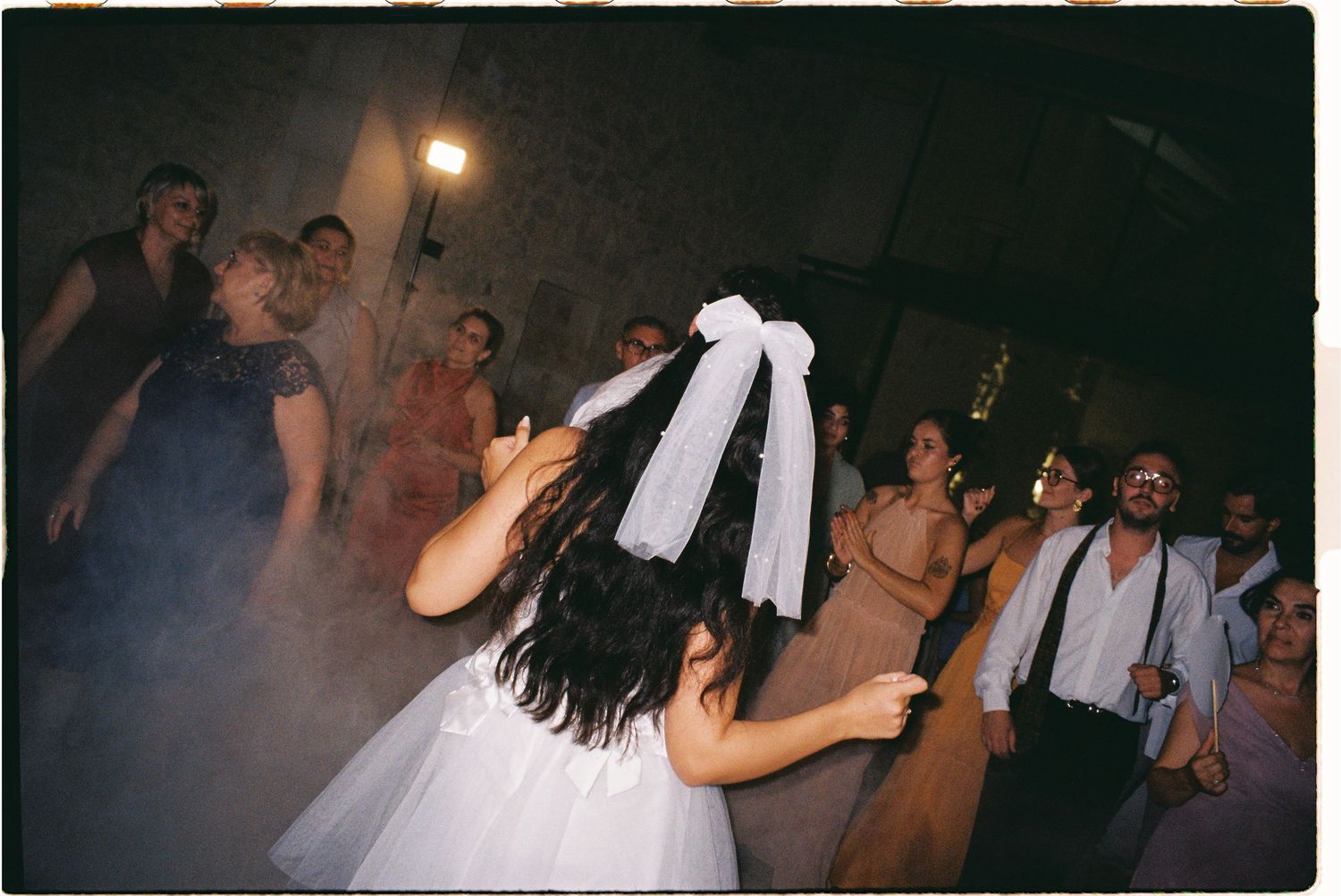 Bride in white dress and veil tossing bouquet to guests at a lively wedding reception dance floor.