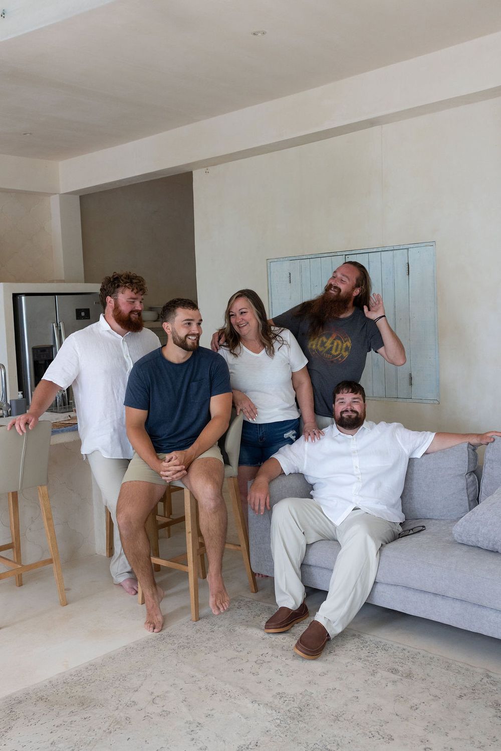 Four friends laughing and relaxing together in a bright modern living room, casually dressed in a cozy home setting.