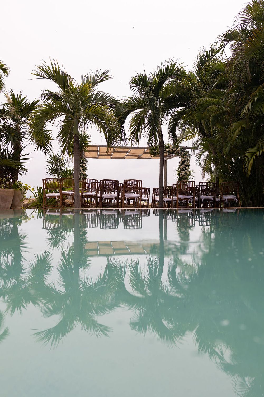Serene pool reflecting palm trees and a white pergola wedding ceremony setup at a tropical Coco B, Isla Mujeres.