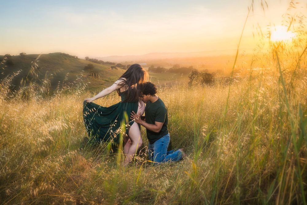 Man kneeling and kissing pregnant woman's belly in a sunlit golden meadow at sunset.