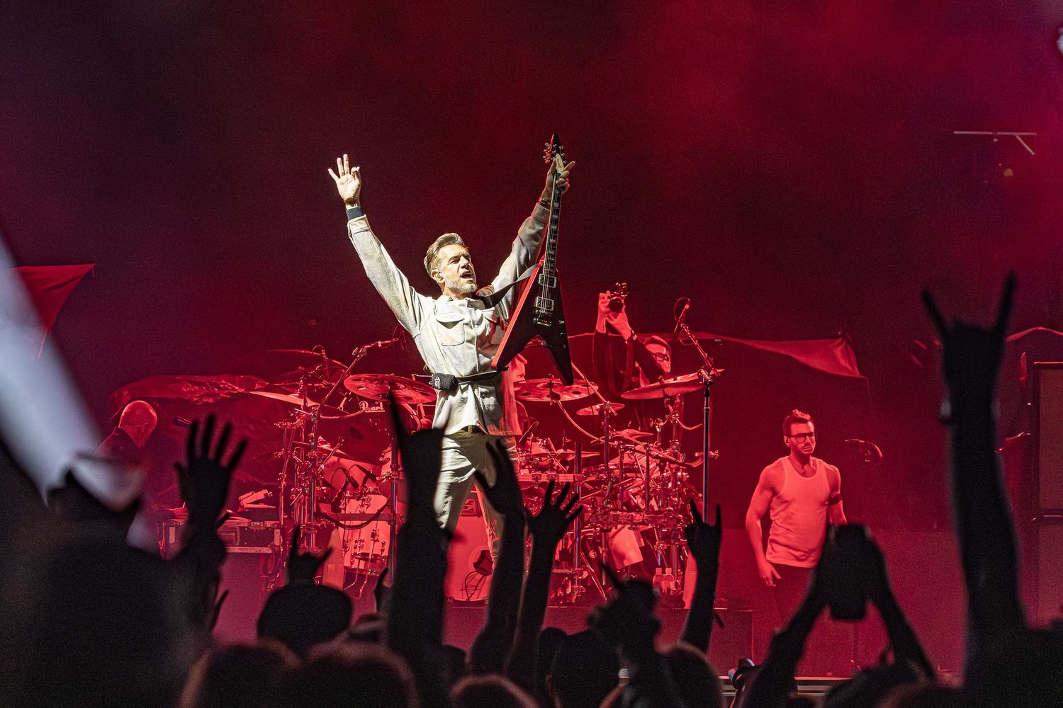 Live music photography of Nick Hexum of 311 holding up a Flying V guitar on stage under red lights in front of a crowd.