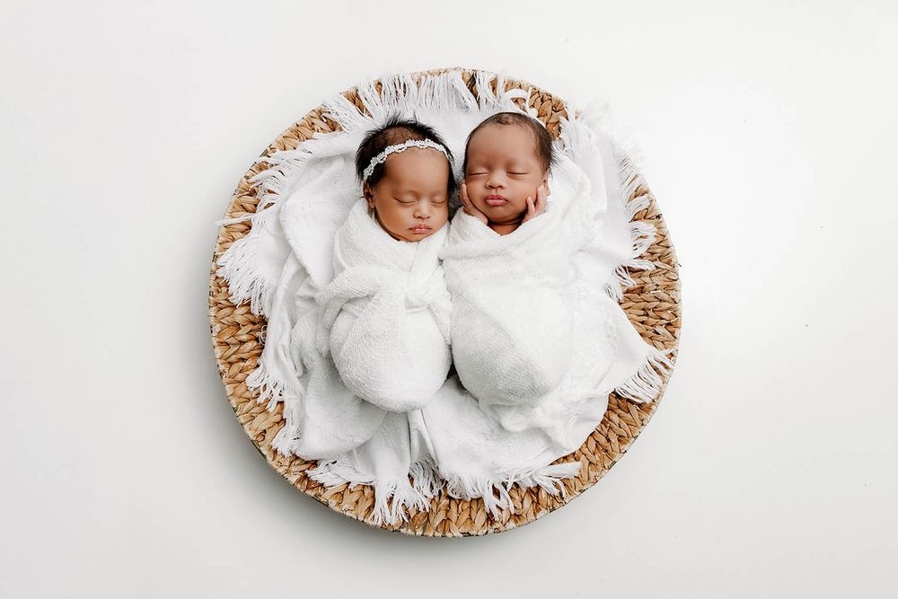 Two sleeping newborn twins swaddled in white blankets in a woven basket by Temescal Valley twin baby photographer.
