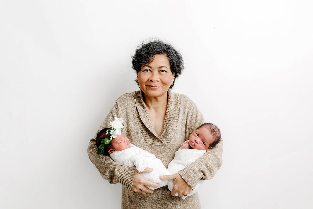 Grandmother smiling while gently holding a sleeping newborn babies by Temescal Valley twin baby photographer.