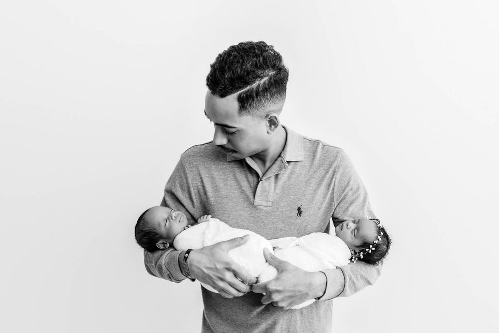 Black and white photo of a father tenderly holding two newborn twins by Temescal Valley twin baby photographer.