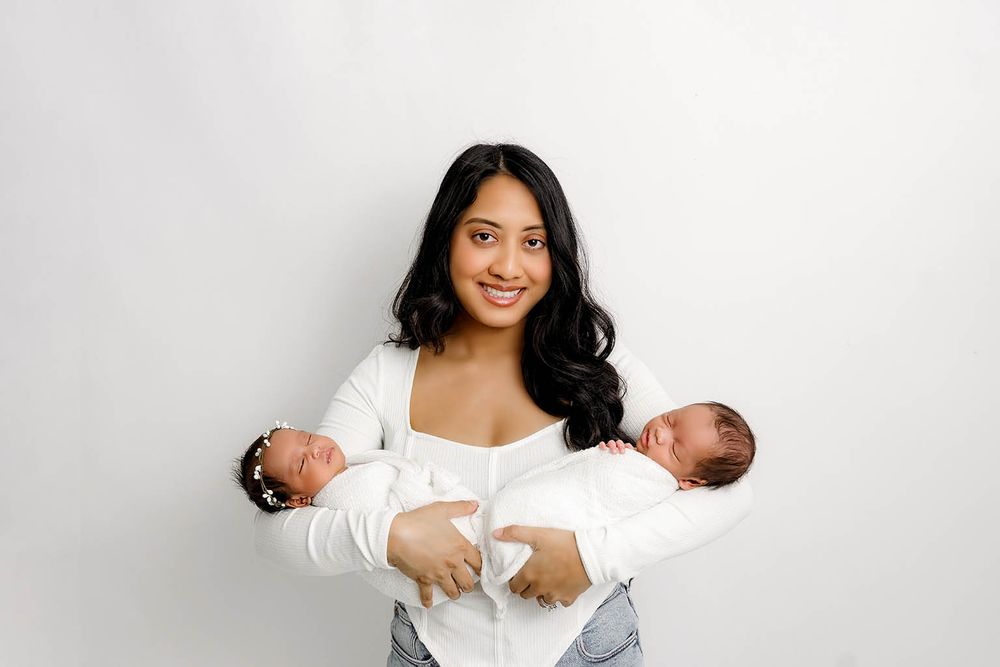 A young woman smiles while holding twin newborn babies in her arms by Temescal Valley twin baby photographer.
