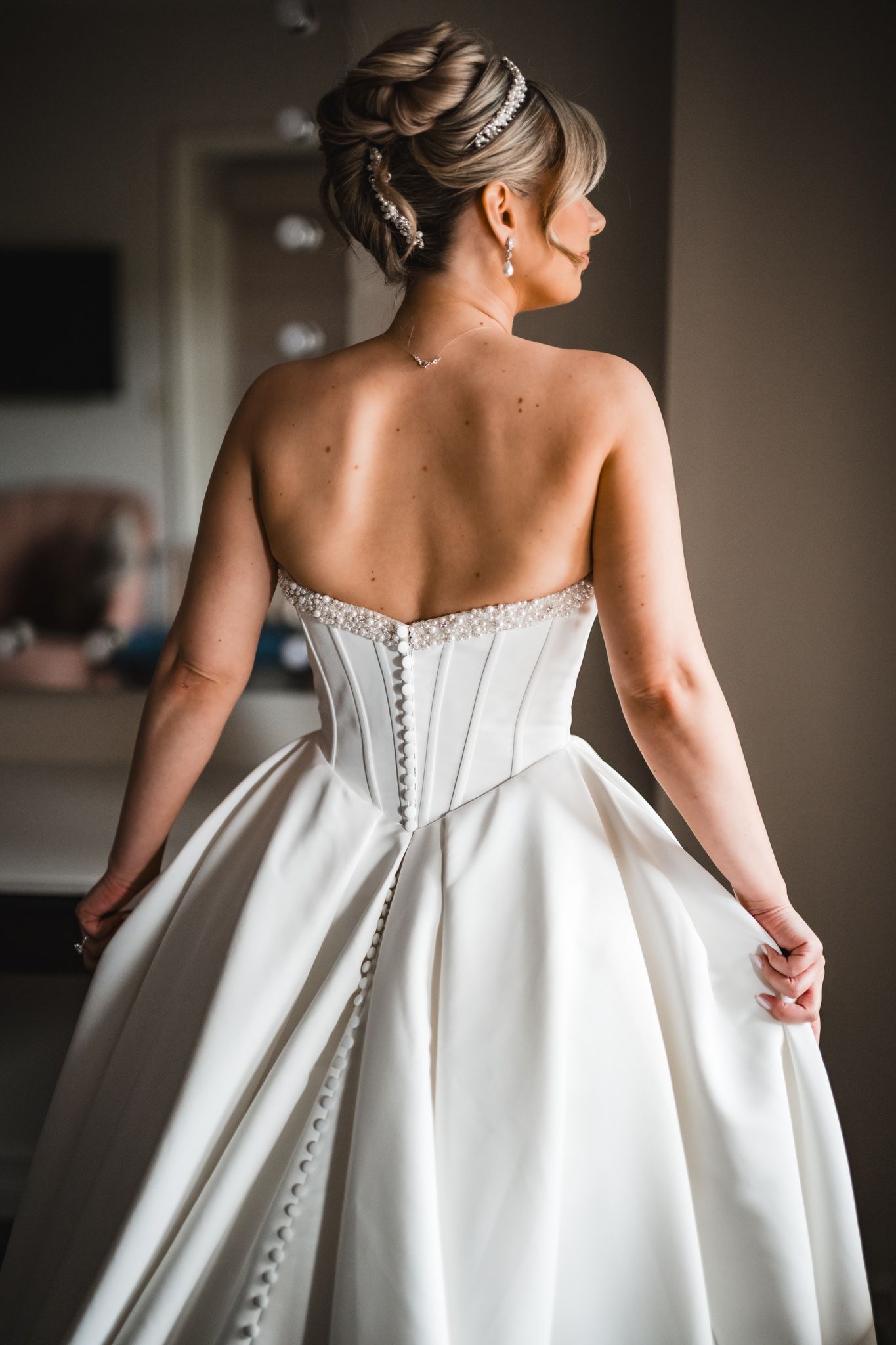 Bride in strapless ball gown with button back corset and elegant updo hairstyle with crystal accessories.