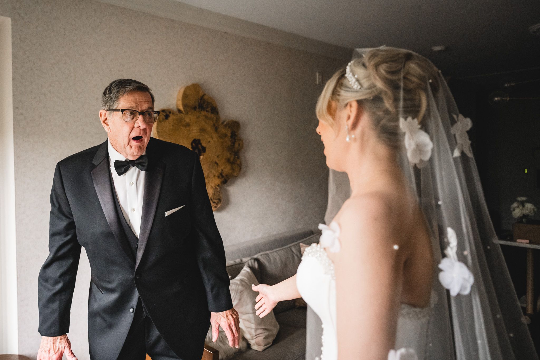 Emotional father reacts with surprise seeing his daughter in wedding dress for first look.