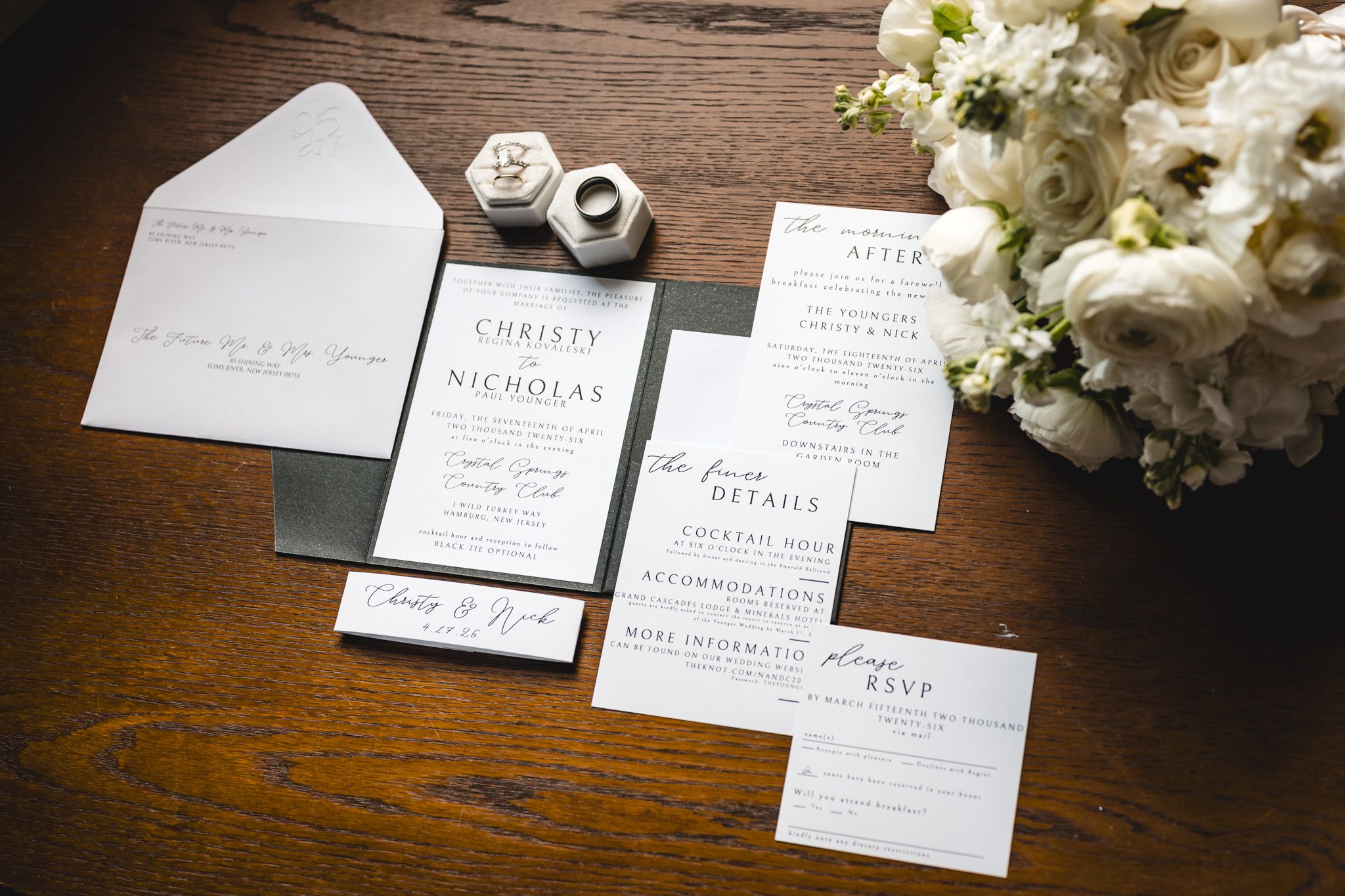 Elegant black and white wedding invitation suite with envelope, RSVP card, and details card on wooden table with white floral bouquet.