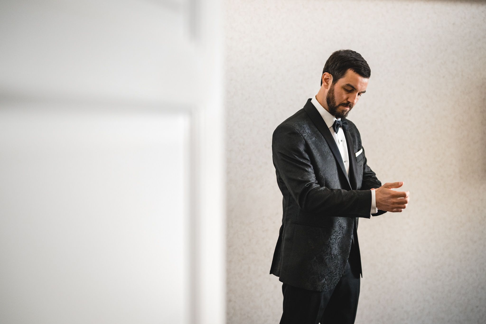 Groom in black tuxedo adjusting cufflinks while getting ready for wedding ceremony.