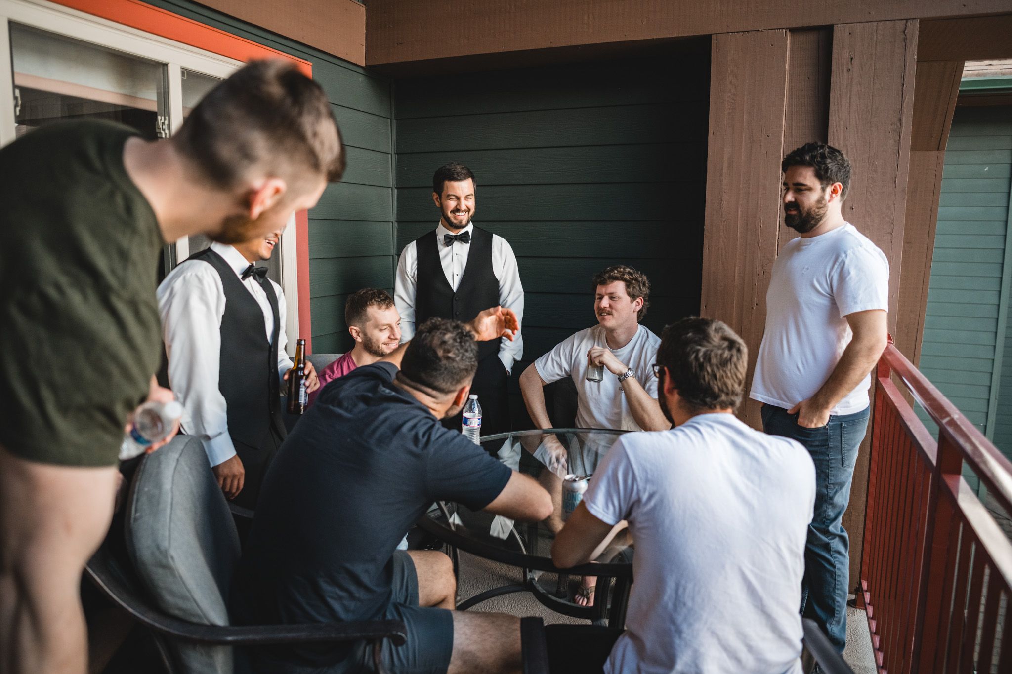 A groom in a vest and bow tie gathers with groomsmen on a balcony before the wedding ceremony.