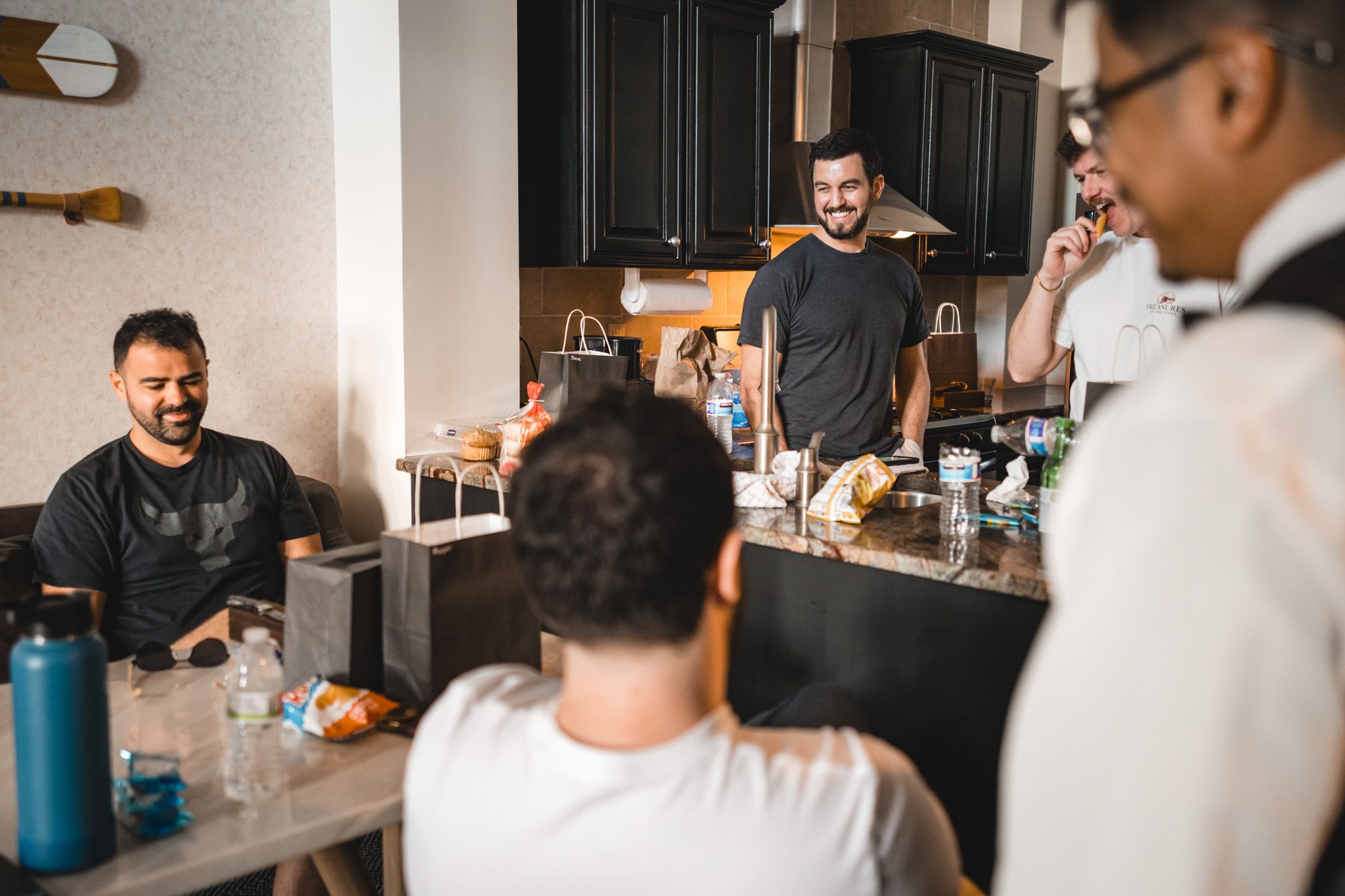 Group of groomsmen laughing and relaxing together in a kitchen during wedding day preparations.