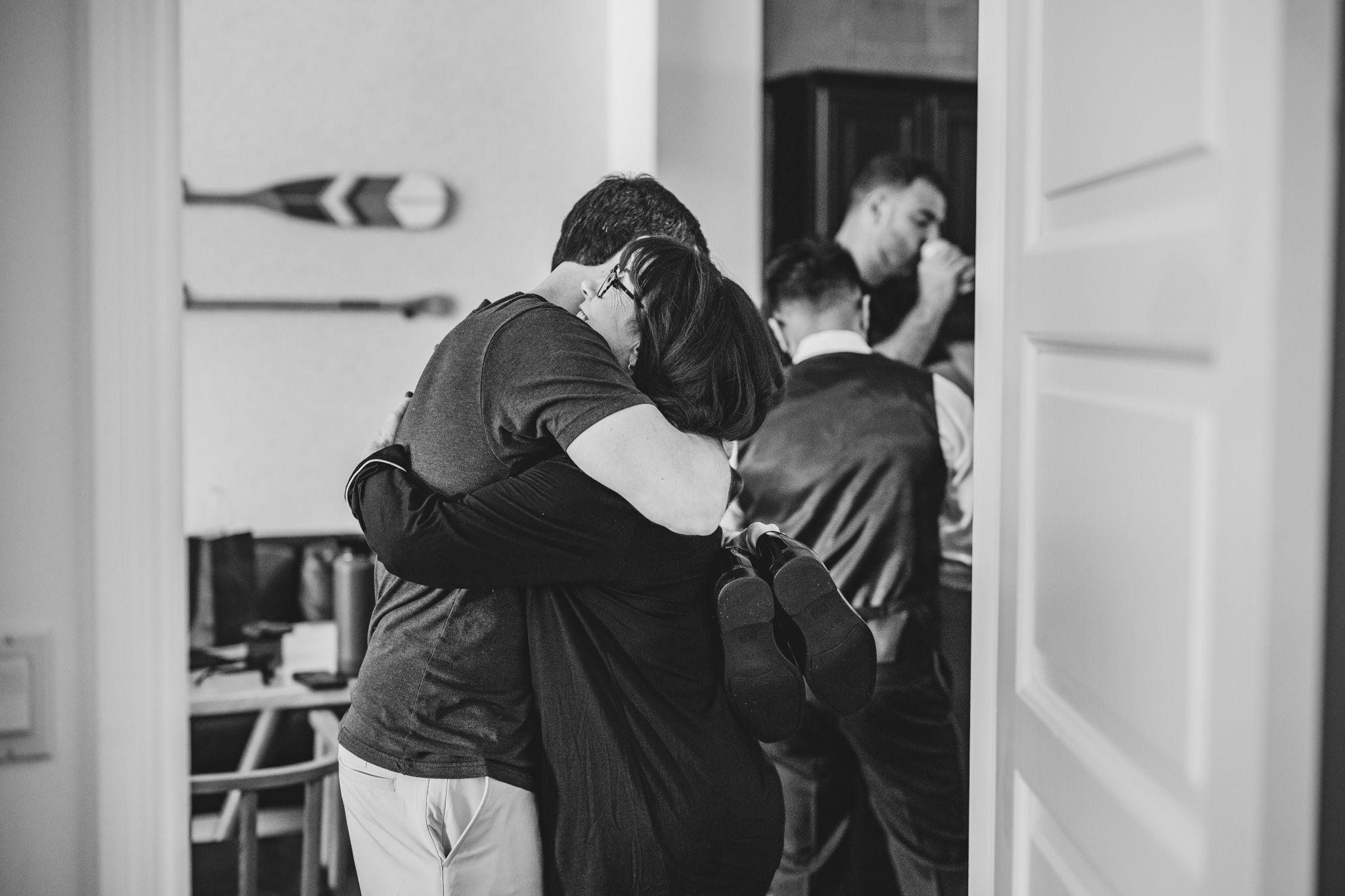 Two men share an emotional hug during a wedding preparation moment captured in black and white photography.