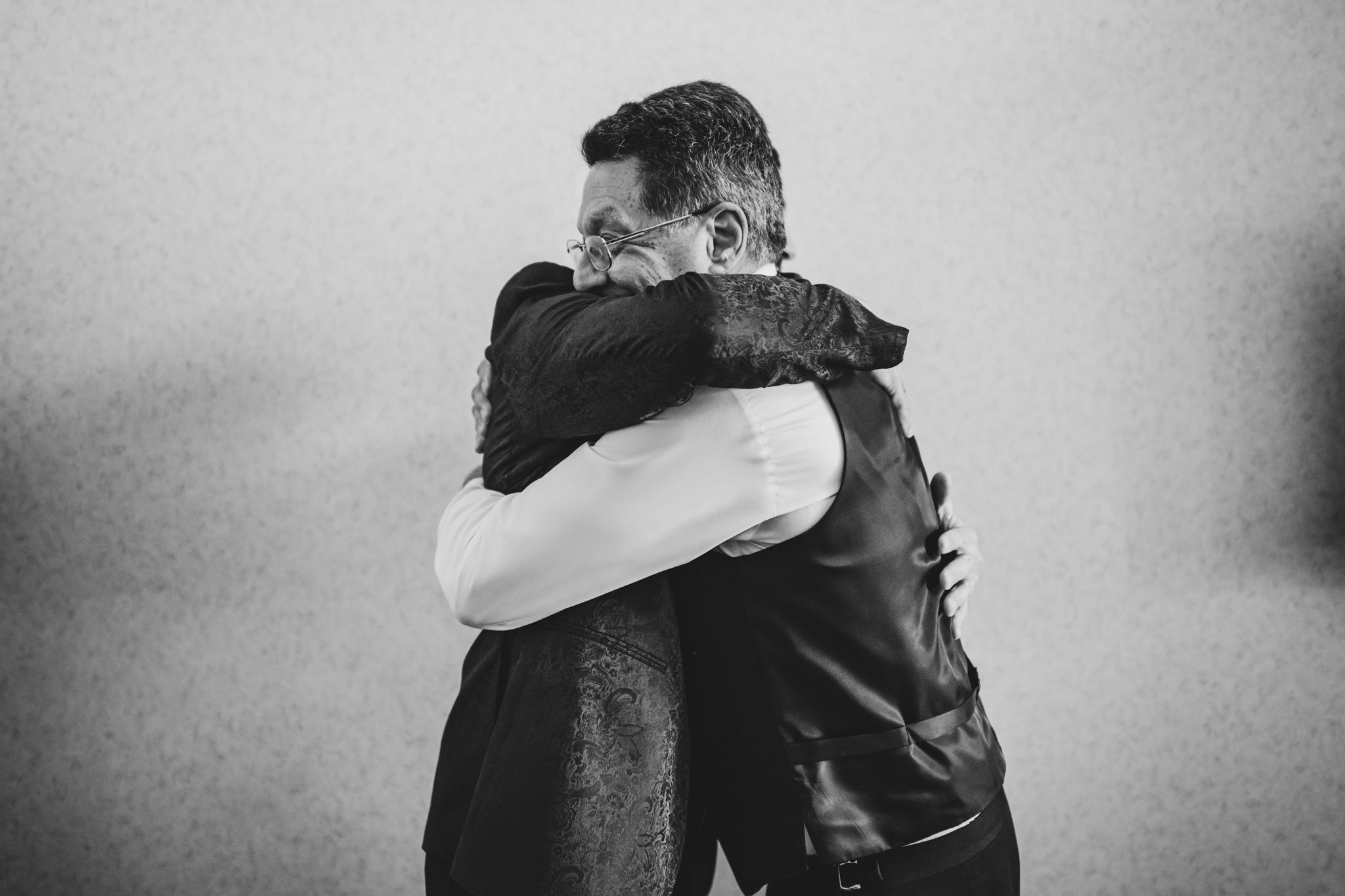Black and white photo of two men sharing an emotional embrace at a wedding.