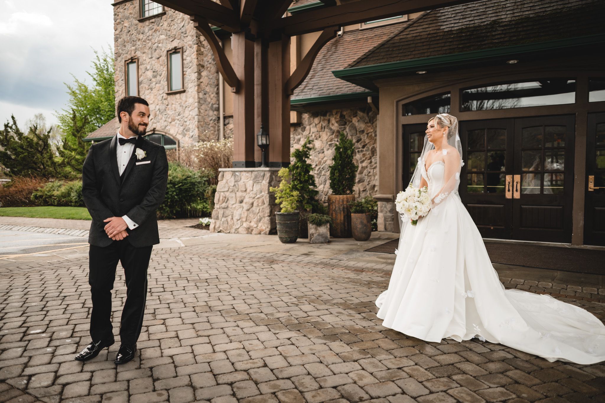 Bride and groom share a first look moment on a cobblestone courtyard outside a stone wedding venue.