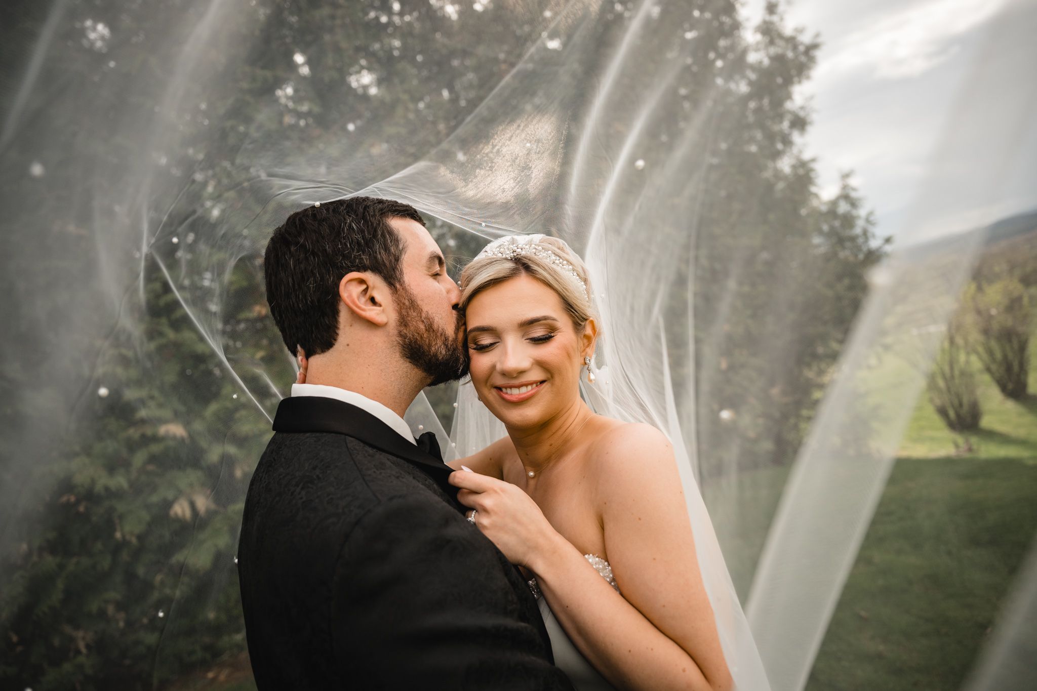 Bride and groom sharing a romantic moment under a flowing veil outdoors at their wedding.
