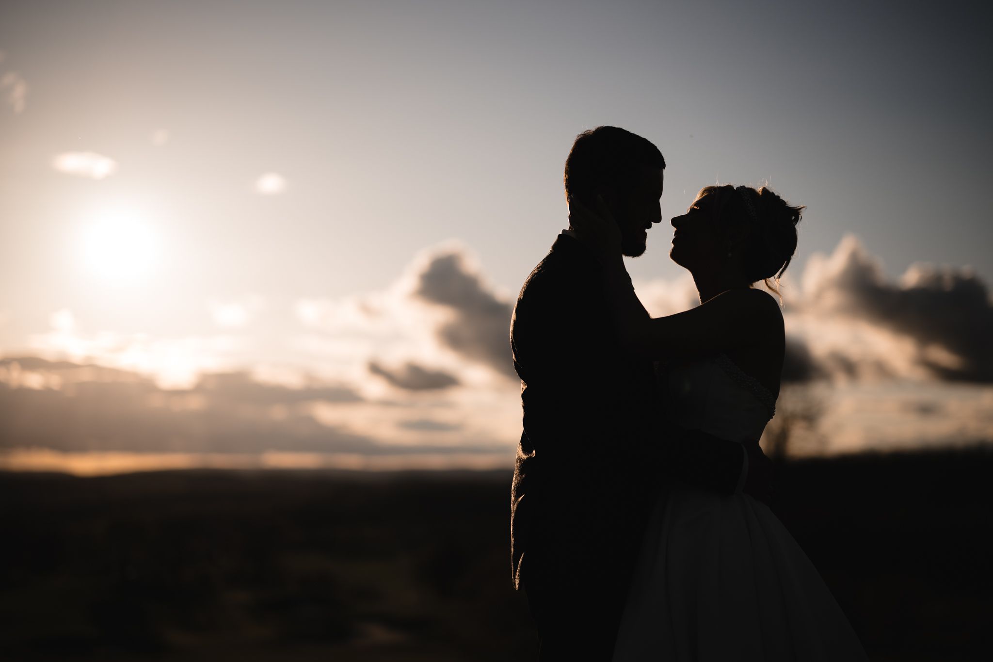 Silhouette of bride and groom embracing at sunset with dramatic clouds in the background.