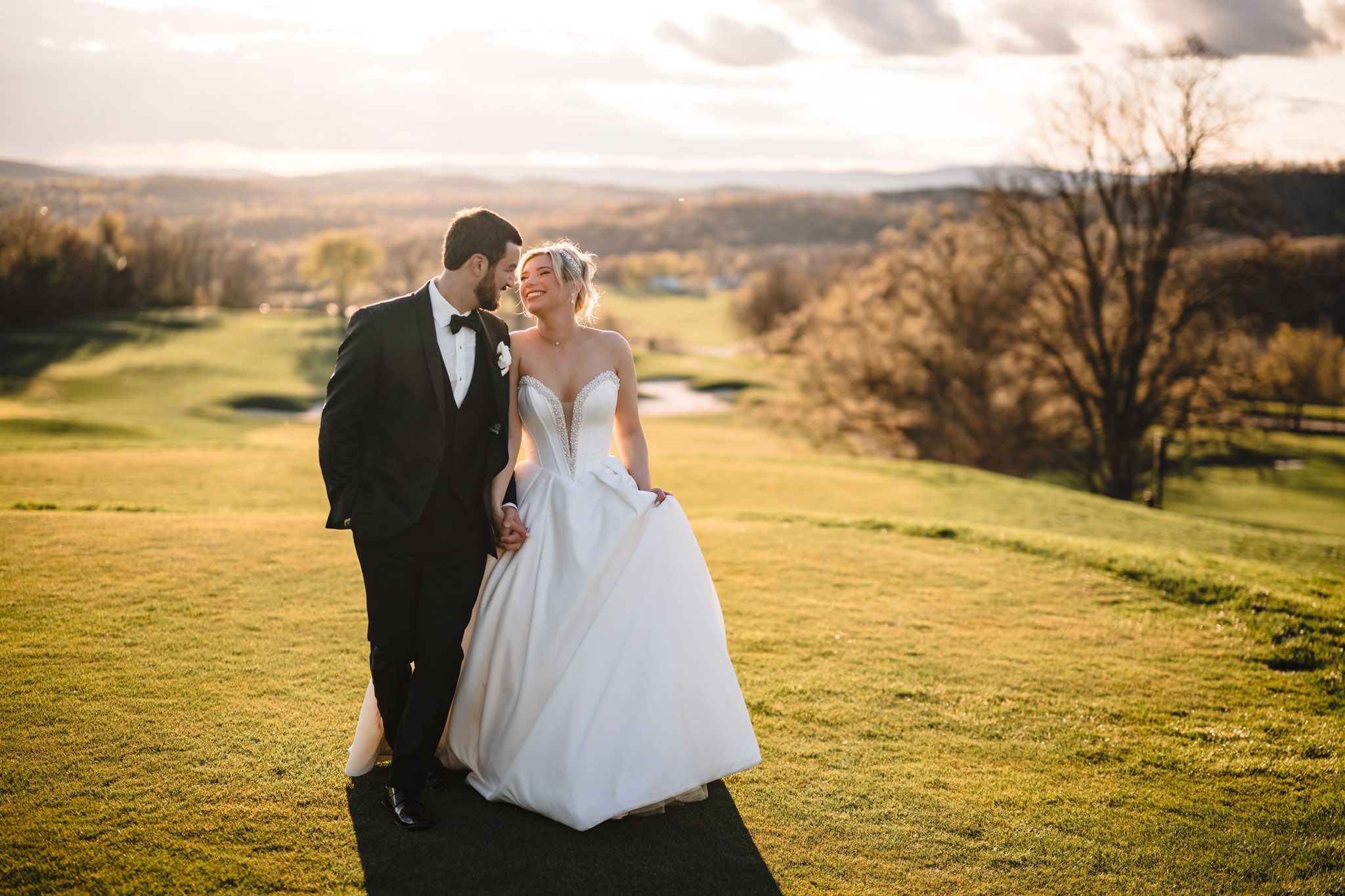 Bride and groom share a romantic sunset kiss on a lush green golf course hillside.