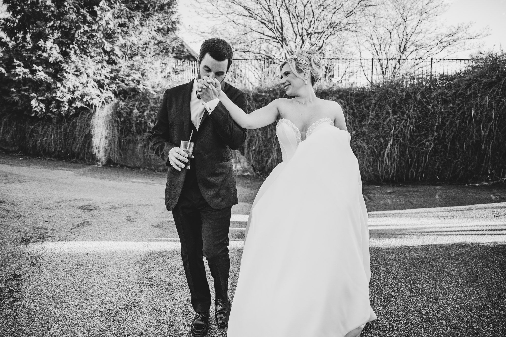 Bride and groom share a playful black and white moment walking along an outdoor path.
