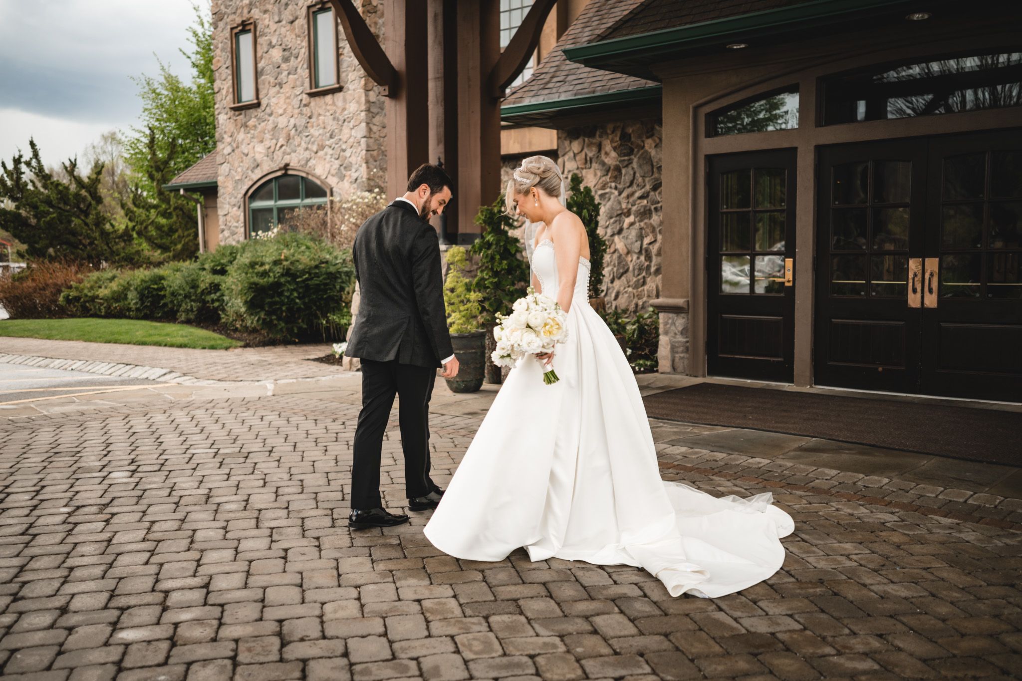 Bride and groom share first look moment on cobblestone path outside stone wedding venue.