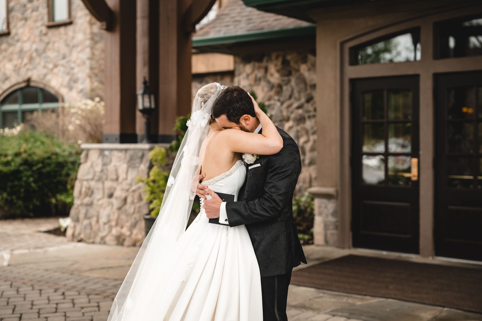 Bride and groom share a romantic embrace outside a stone building on their wedding day.