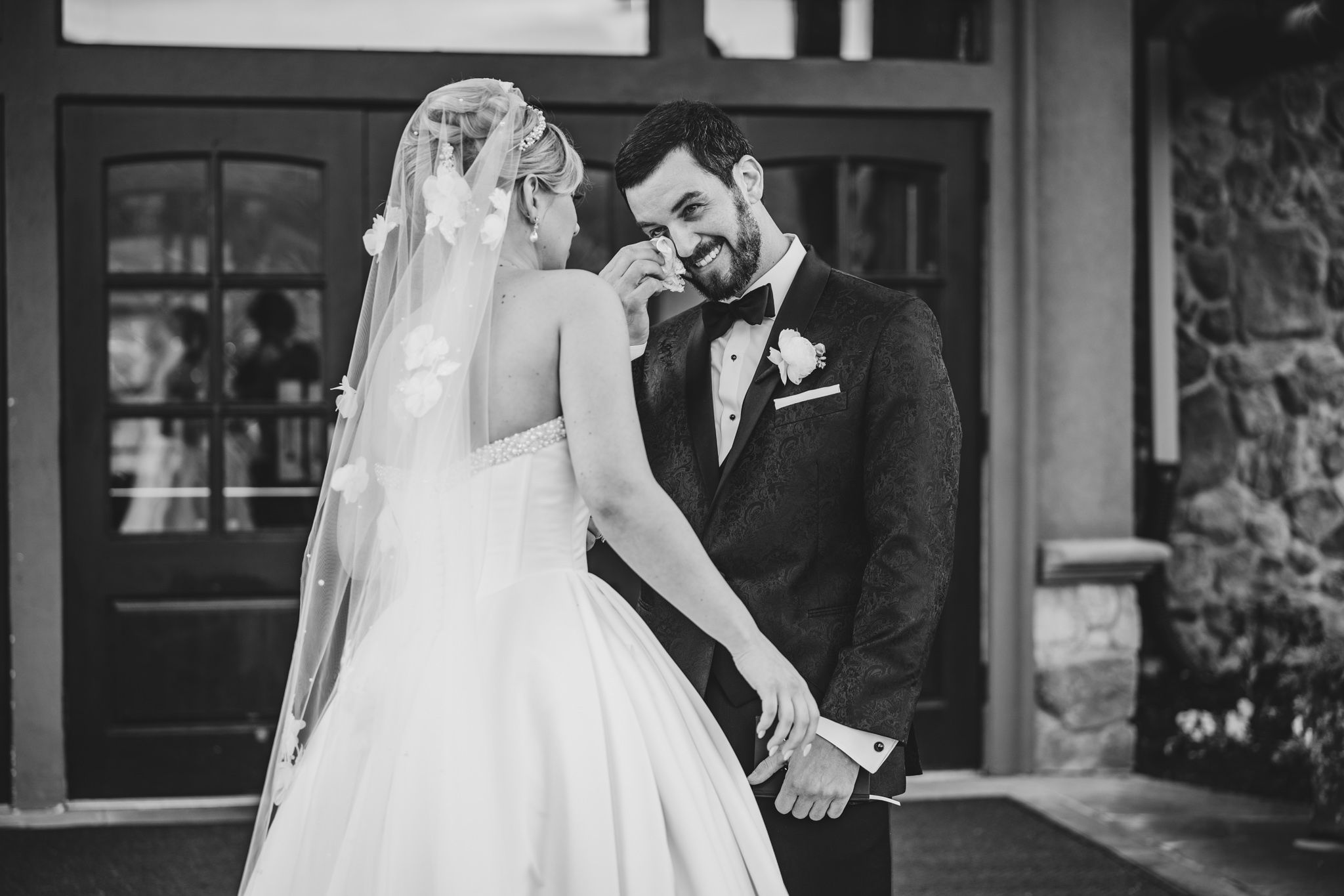 Emotional black and white photo of bride and groom sharing an intimate moment outside wedding venue doors.