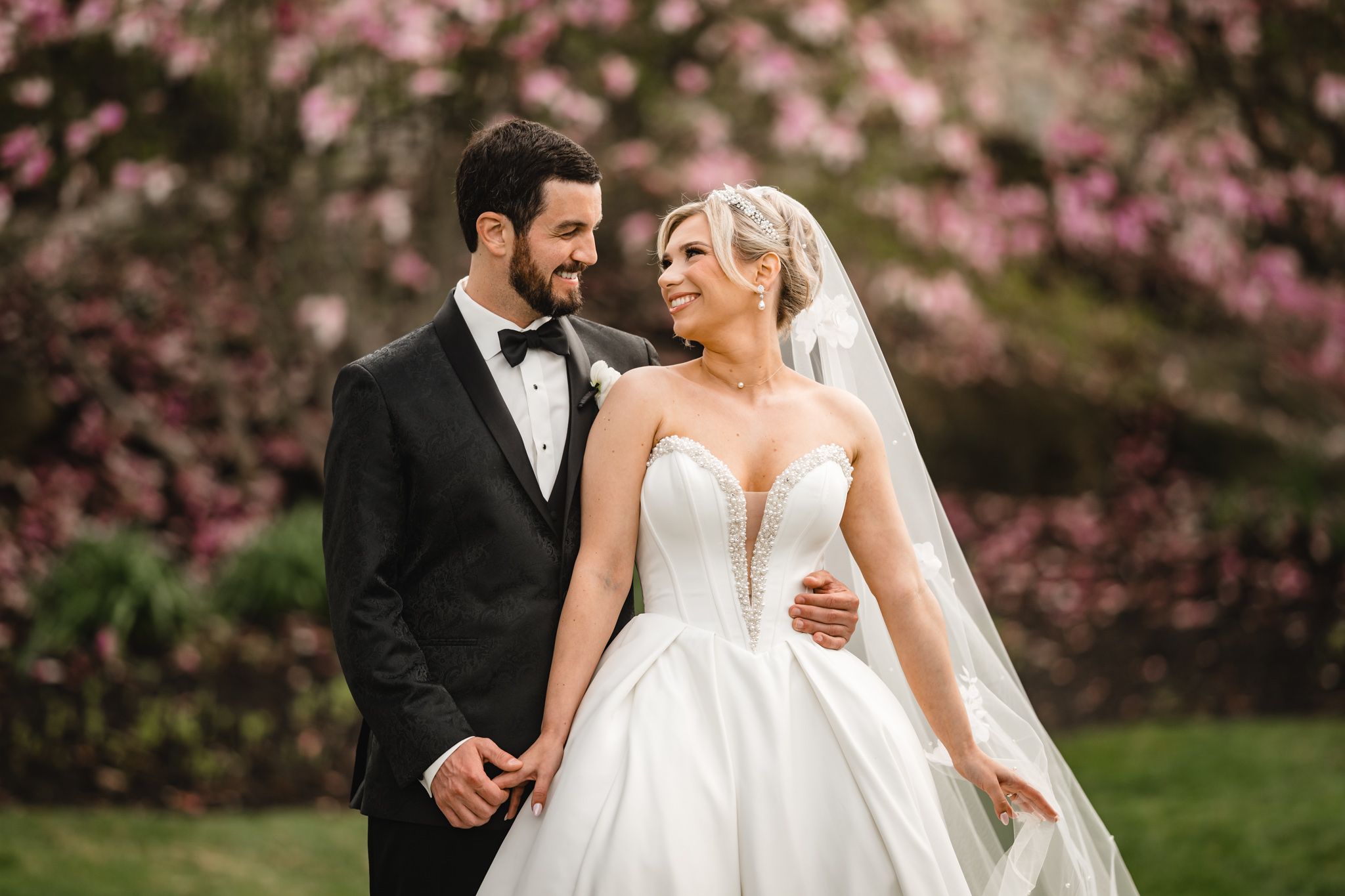 Bride and groom share a romantic moment outdoors with pink cherry blossoms in the background.