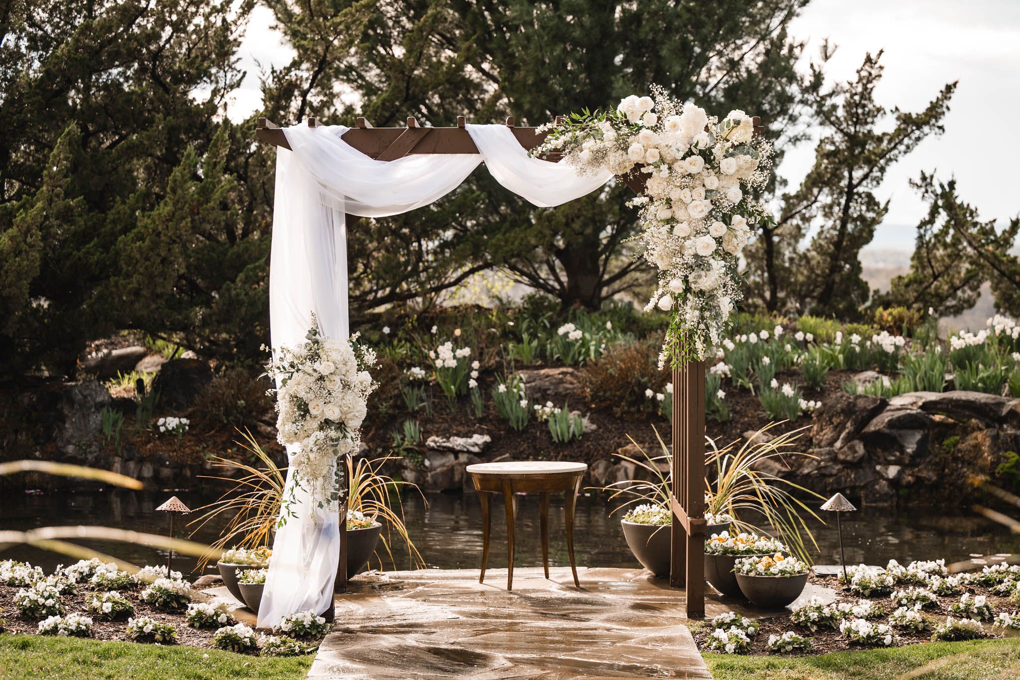 Elegant outdoor wedding arch adorned with white flowers and draped fabric, set in a lush garden ceremony space.