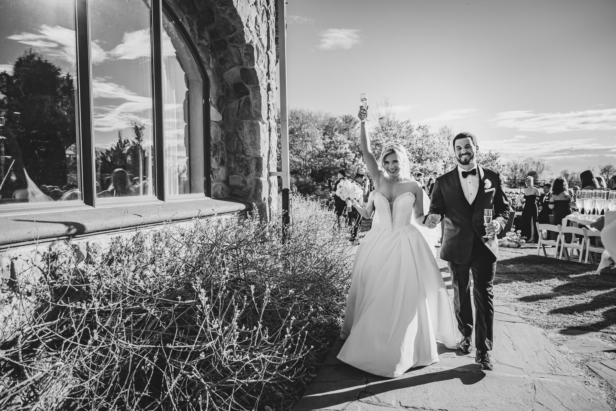 Joyful newlyweds celebrate with raised arms after their outdoor wedding ceremony in black and white photo.