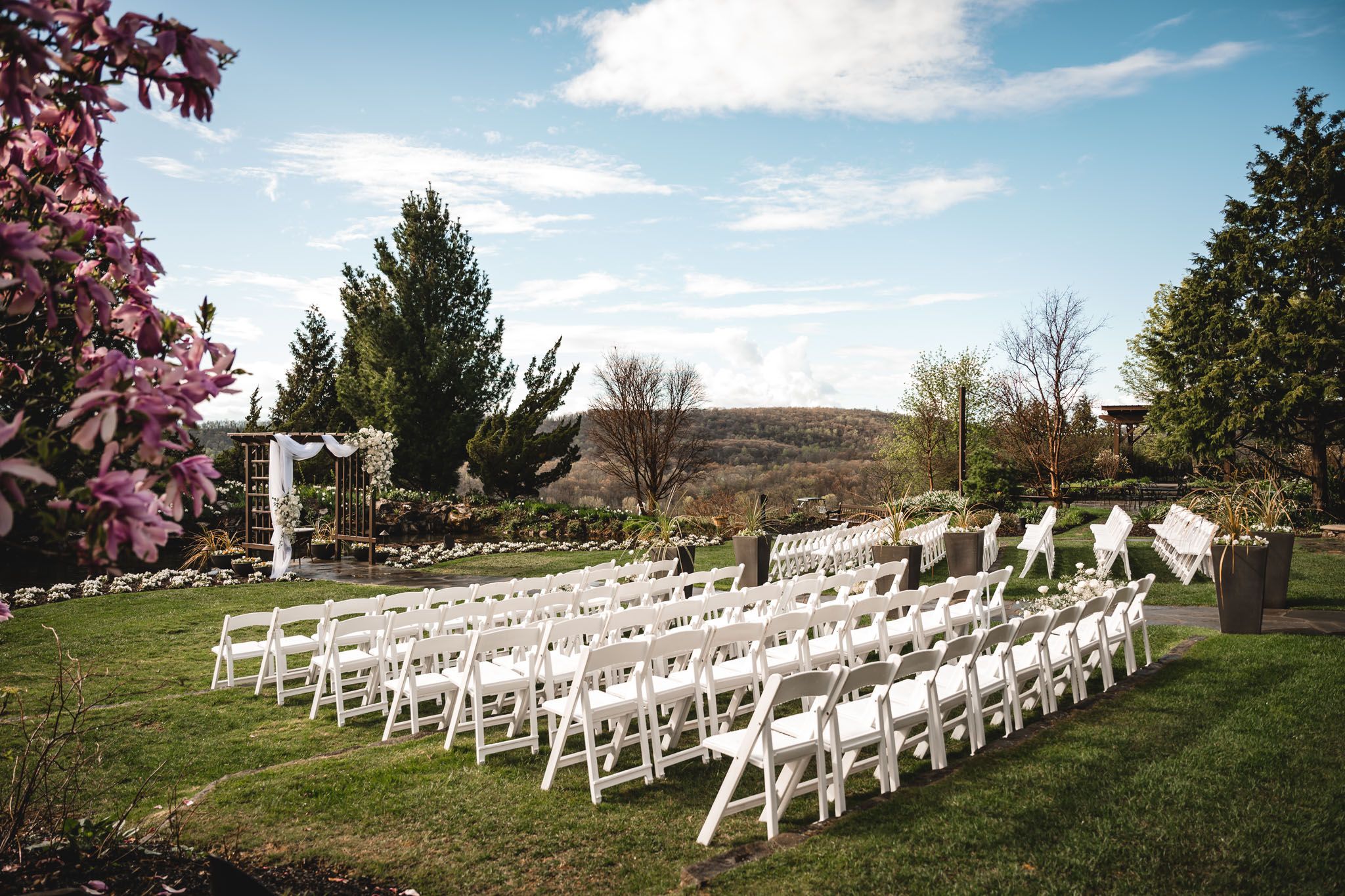 Rows of white chairs set up for an outdoor wedding ceremony with mountain views and blooming trees.