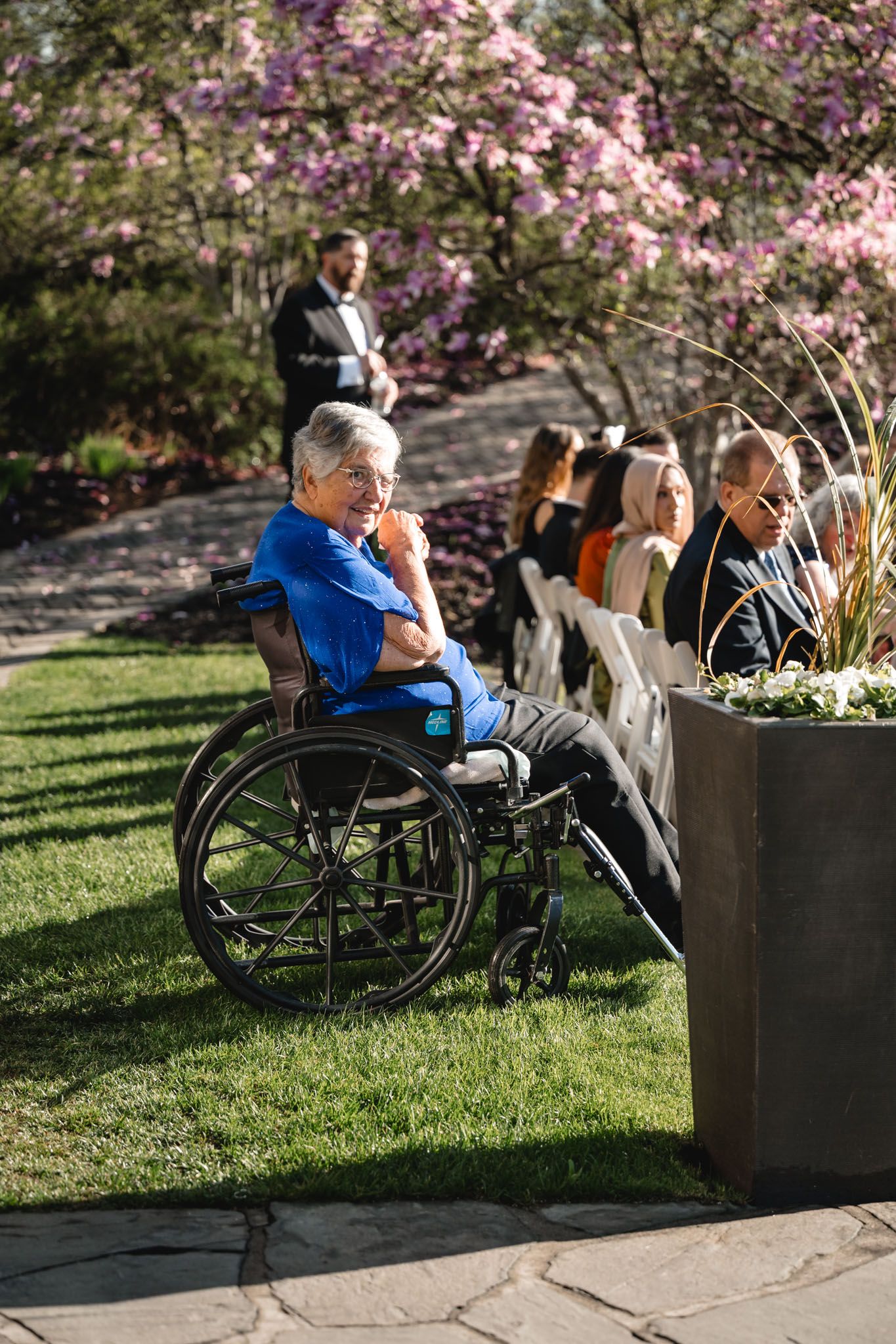Wedding guest in wheelchair enjoying an outdoor ceremony surrounded by blooming pink trees.