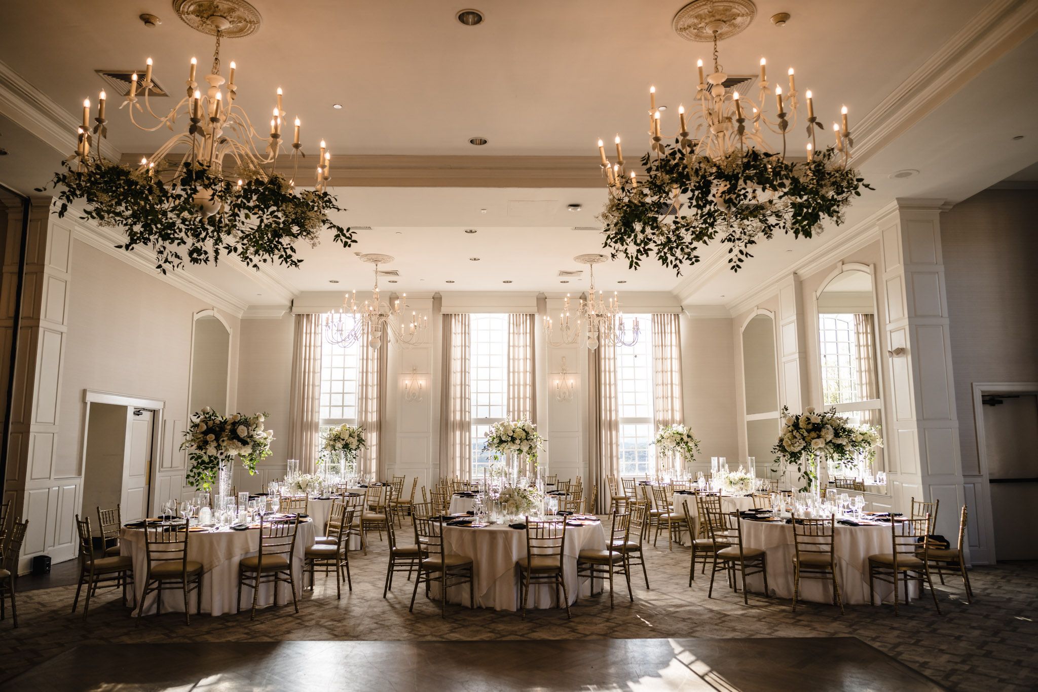 Elegant wedding reception hall with floral chandeliers, tall centerpieces, and chiavari chairs.