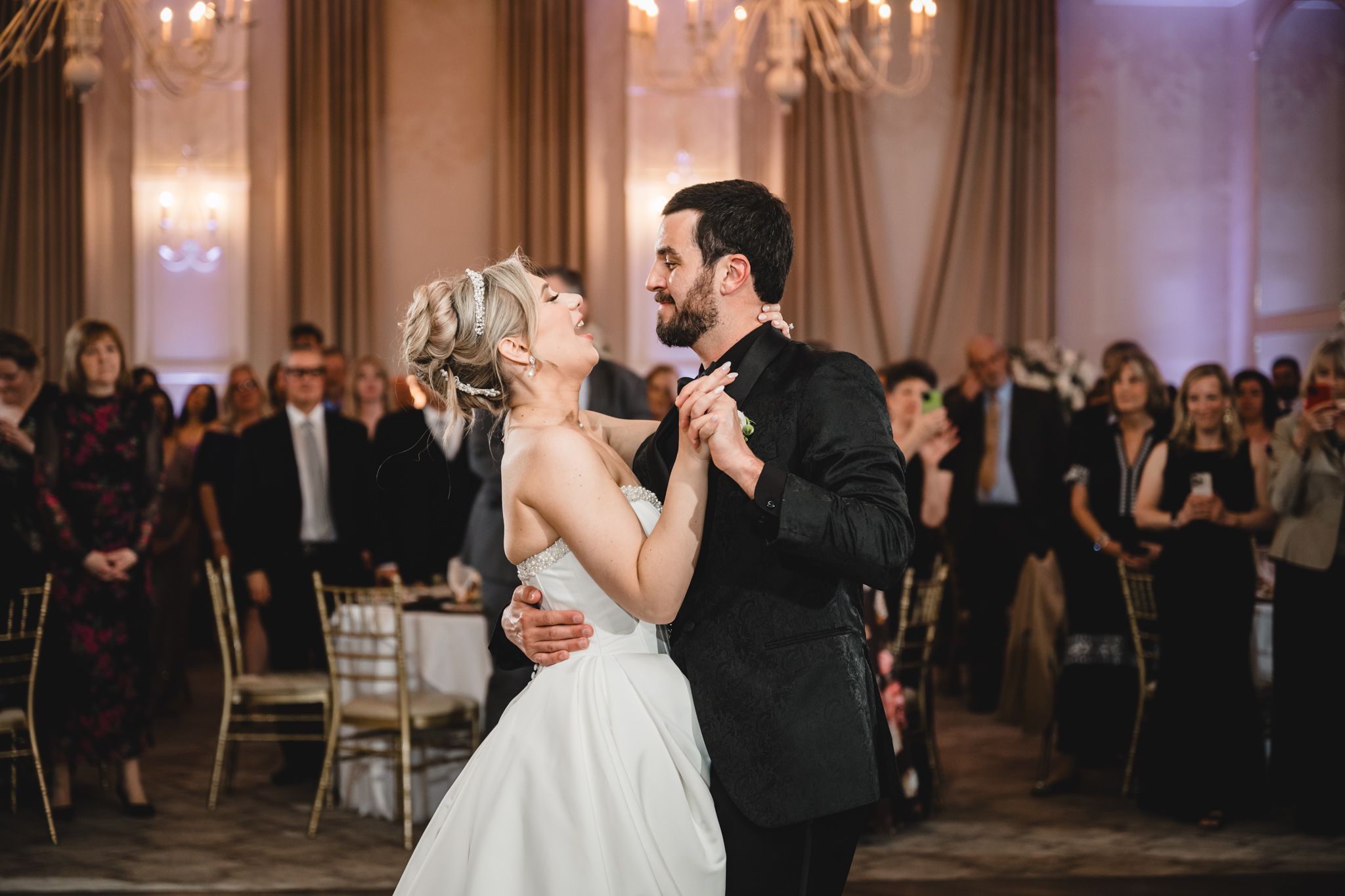 Bride and groom share an intimate first dance moment while guests watch in a elegant ballroom.