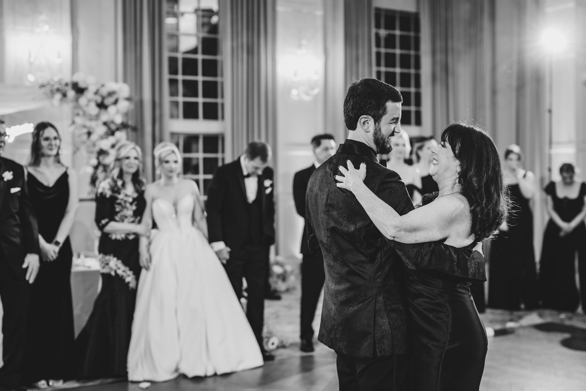 Groom shares emotional mother-son dance in black and white photo at classic wedding reception.