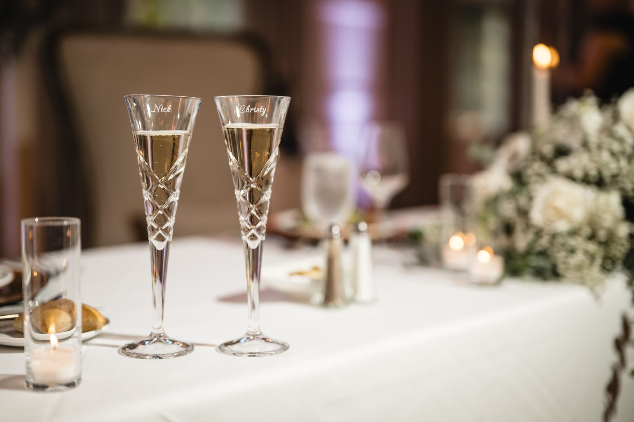 Two elegant crystal champagne flutes filled with sparkling wine on a white wedding reception table.