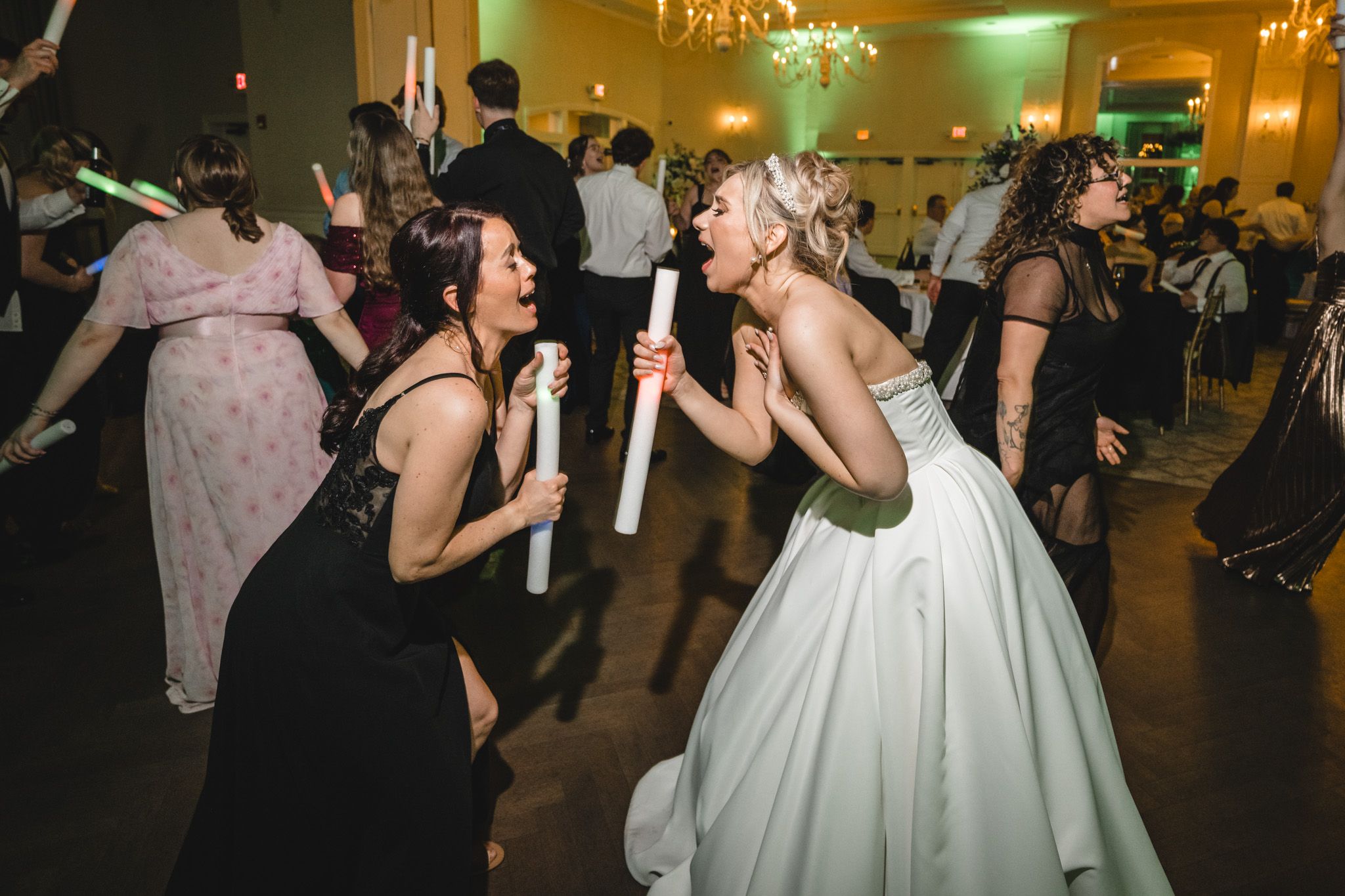Bride and guest dancing joyfully with glow sticks at a lively wedding reception celebration.
