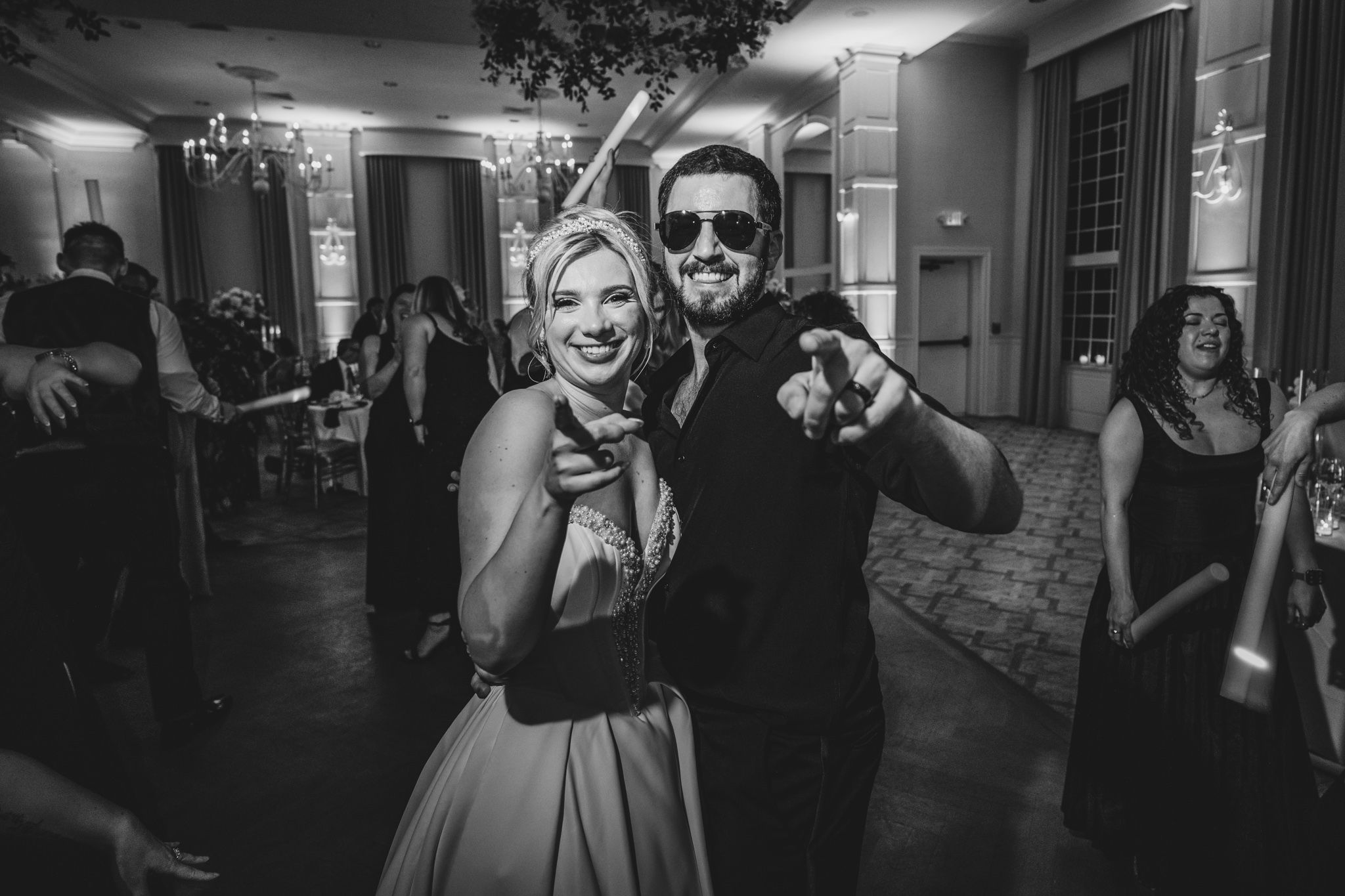 Bride and groom pose playfully in black and white photo on wedding reception dance floor.