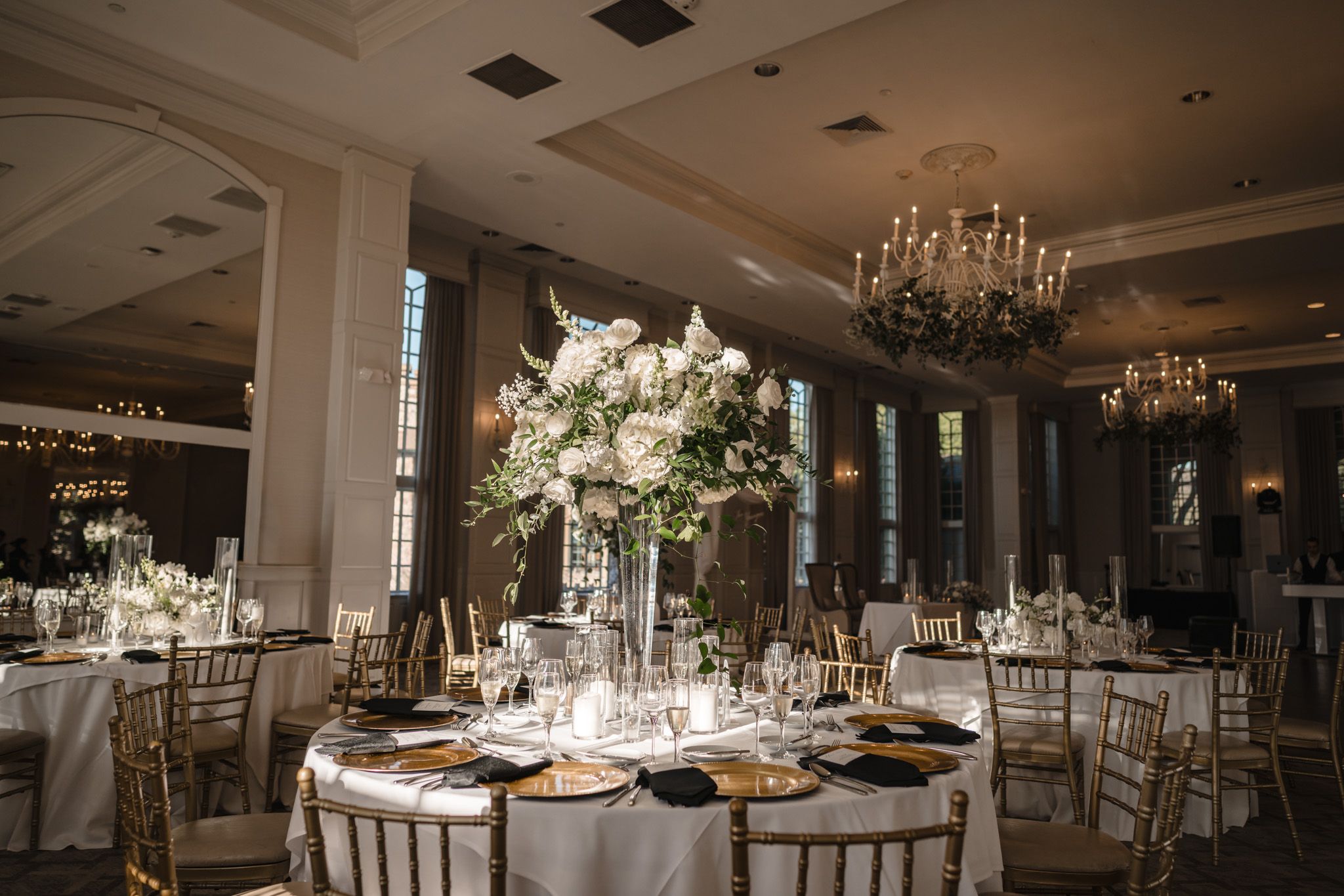 Elegant wedding reception ballroom with tall floral centerpieces, gold chiavari chairs, and crystal chandeliers.