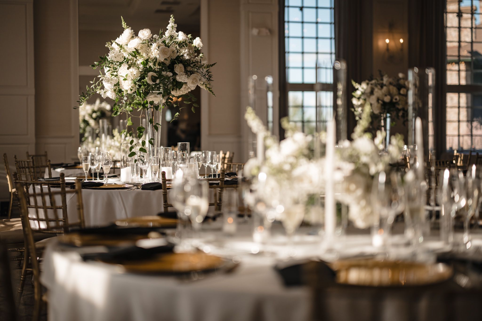 Luxurious wedding reception tables with white floral arrangements, gold chargers, and crystal glasses.