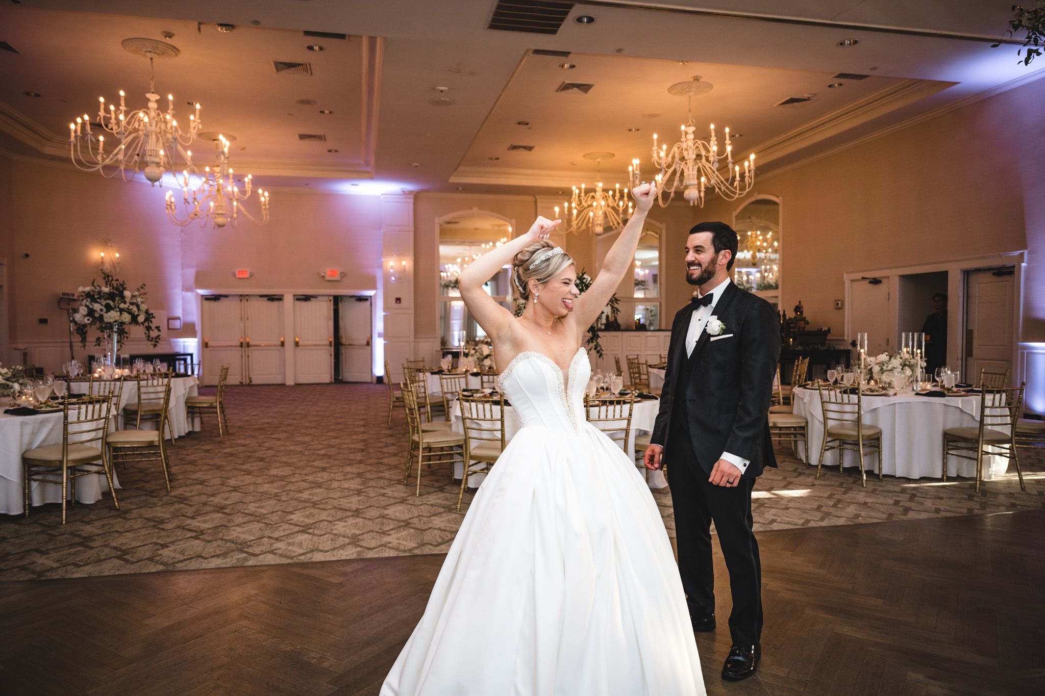 Bride and groom make a grand entrance into a glamorous ballroom with chandeliers at their reception.