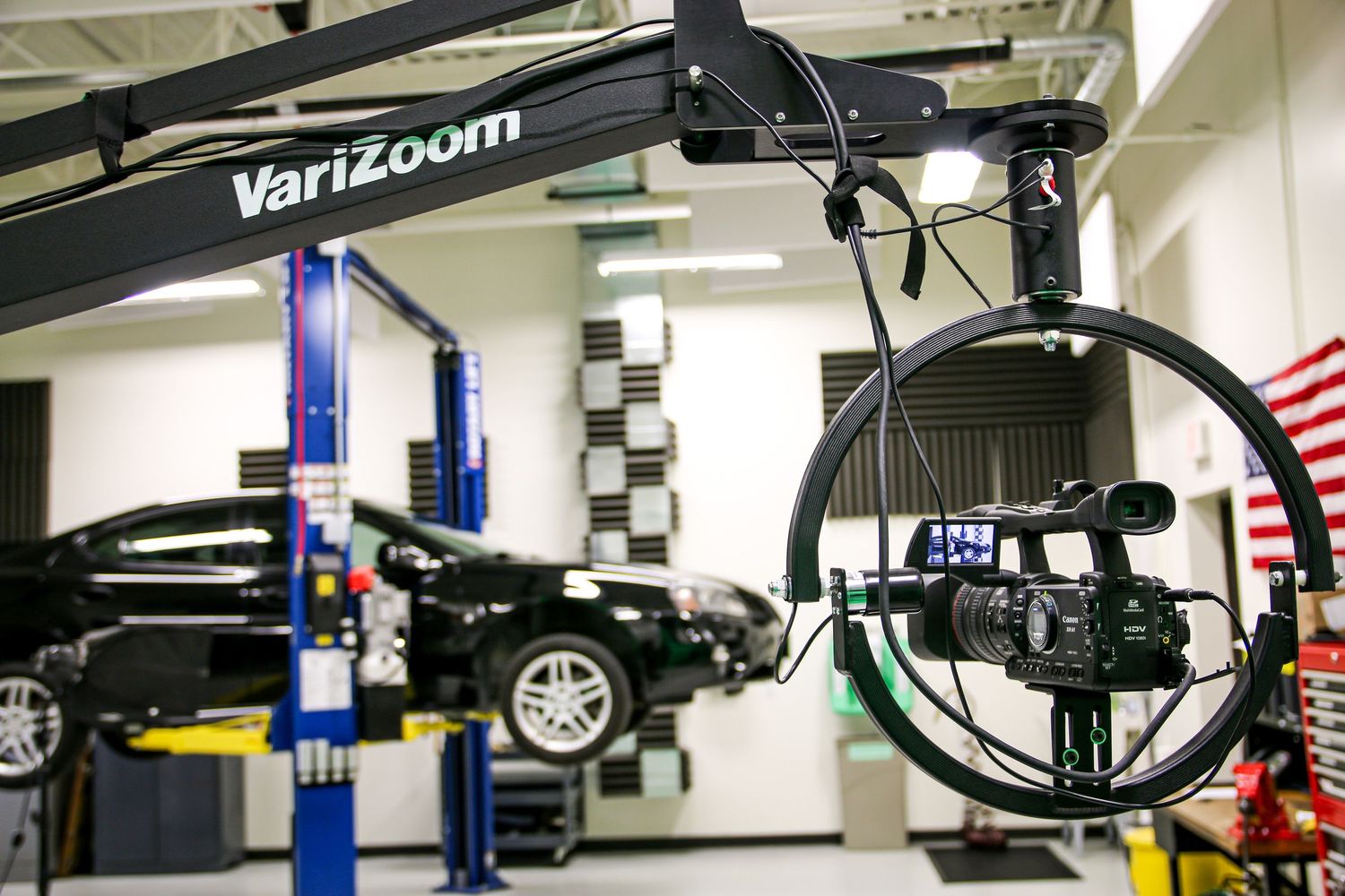 VariZoom camera crane jib arm with video camera in an auto repair shop with cars on lifts.