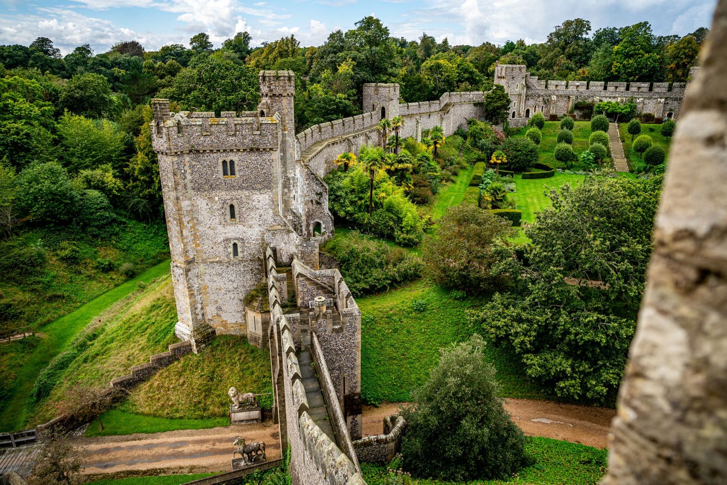 Aerial view of a medieval stone Arundel castle with battlements, towers, and lush green gardens surrounded by ancient walls in England