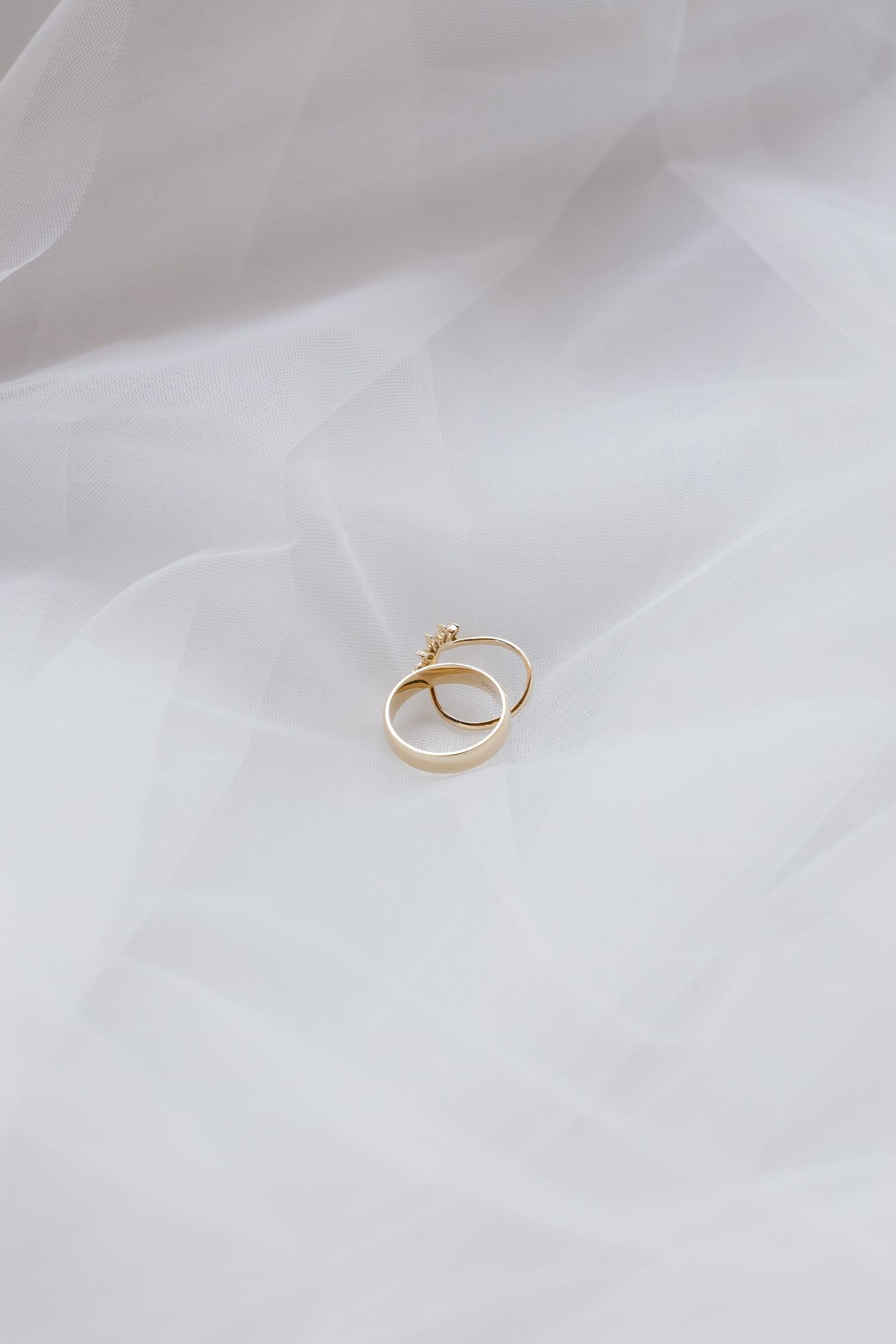 Gold wedding rings photographed on white tulle fabric in minimalist style.