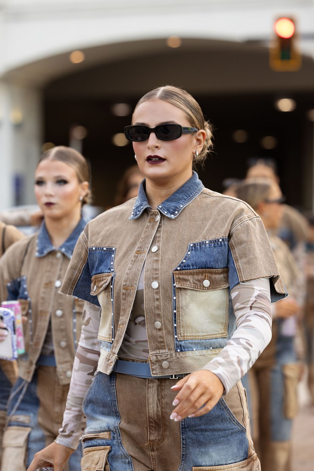 Female dancers marching in matching denim patchwork outfits with dark lipstick and black sunglasses.