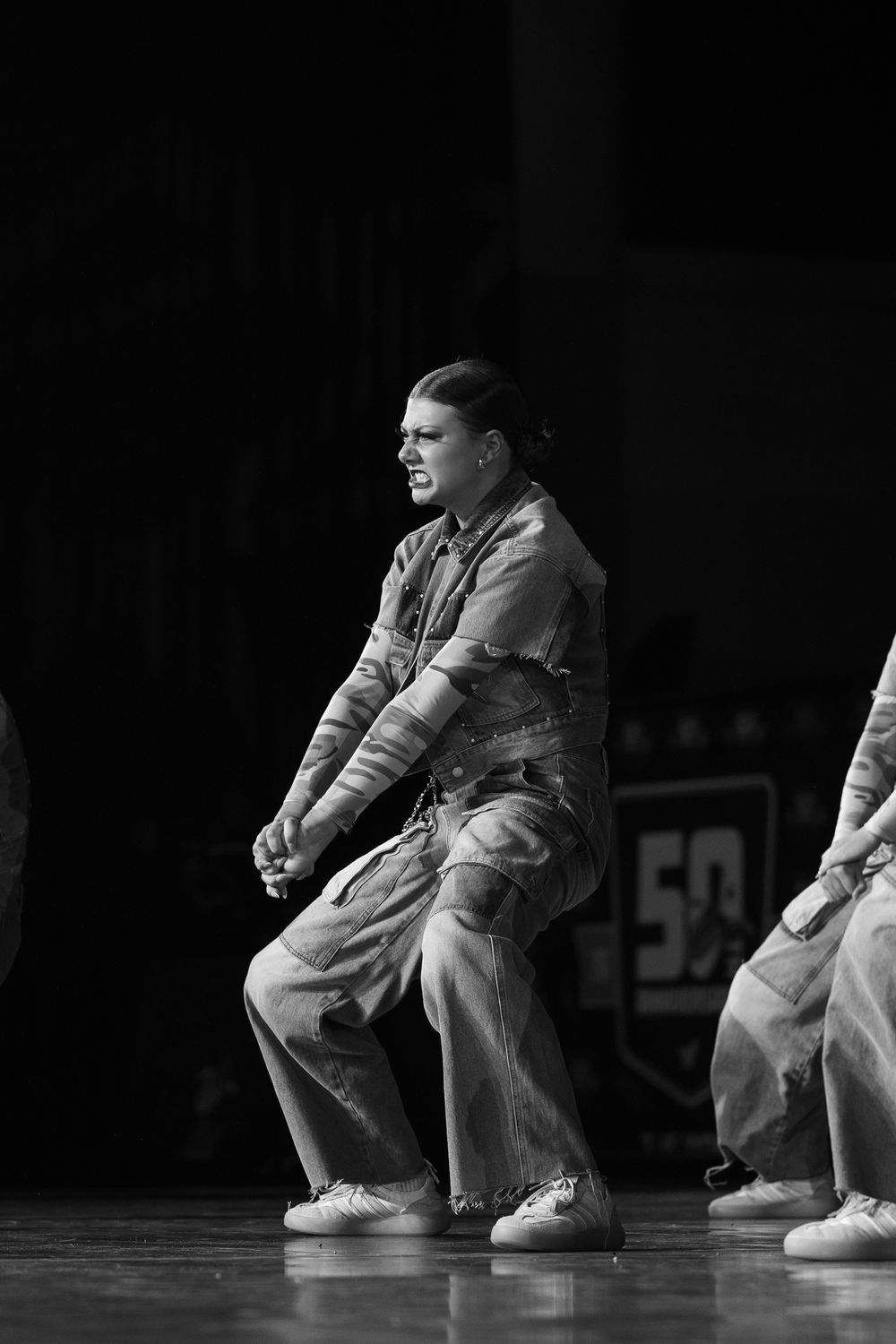 Black and white photo of a dancer performing on stage in baggy jeans and jacket during a hip-hop dance competition.