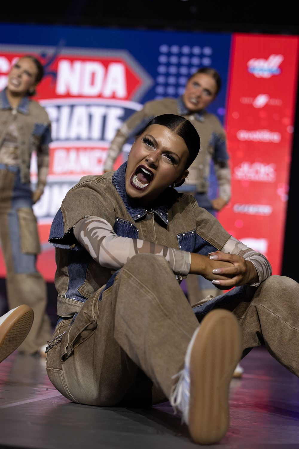 Dancer performs an expressive floor routine at NDA Collegiate Dance Championships in denim and tan outfit.