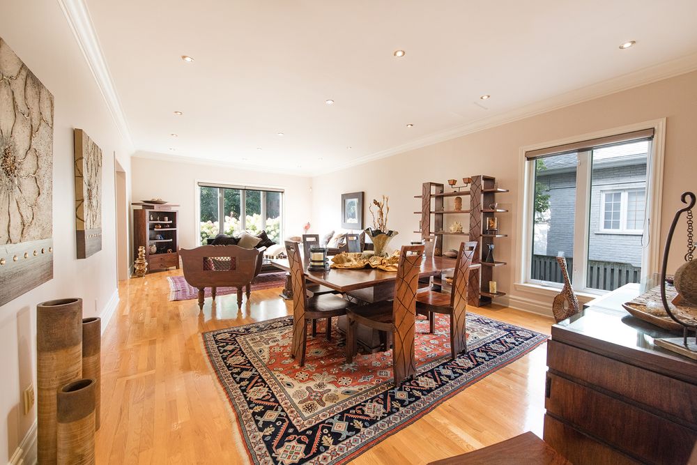 Elegant dining room with hardwood floors, Persian rug, wooden furniture, open shelving, and large windows with natural light.